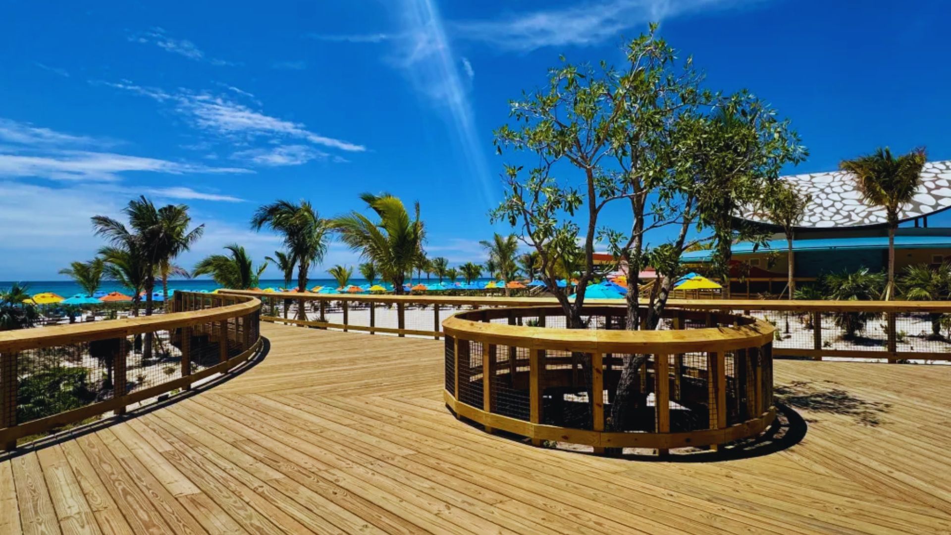 A scenic view of the boardwalk at a beach resort, lined with palm trees and overlooking the sandy beach.