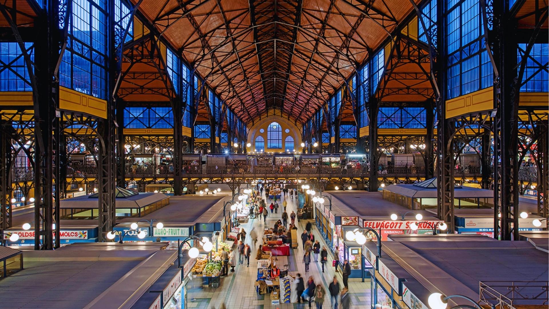 Interior of a busy train station with people walking and waiting, showcasing various shops and information displays.