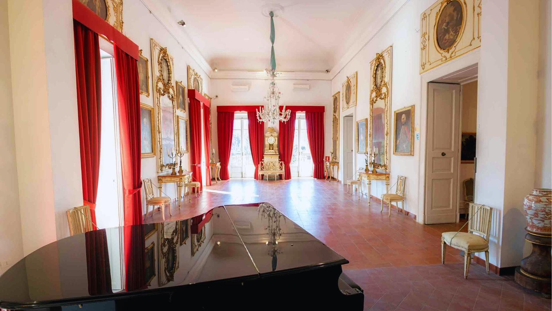 A long hallway adorned with red curtains, featuring a grand piano at the end, creating an elegant atmosphere.
