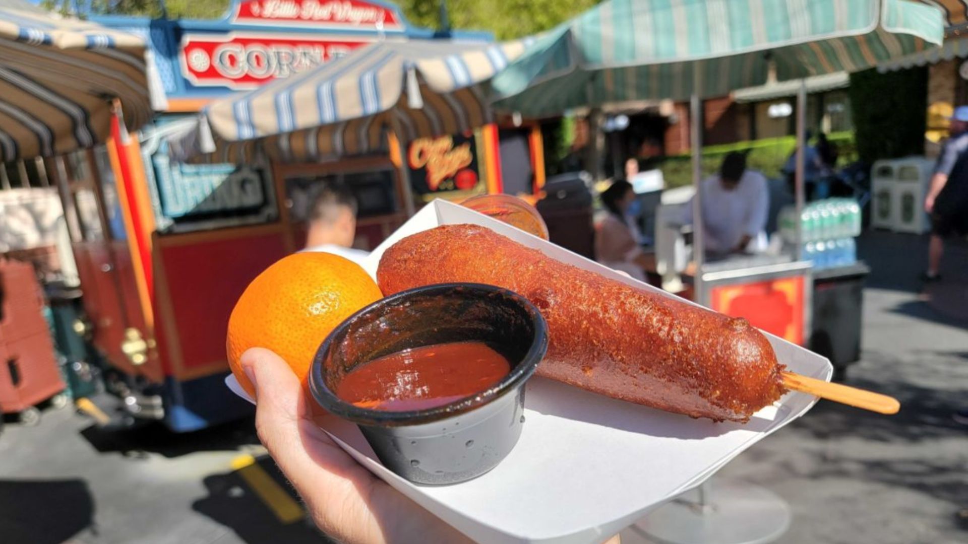 In front of a food truck, an individual enjoys a hot dog and a drink, showcasing a casual dining experience.