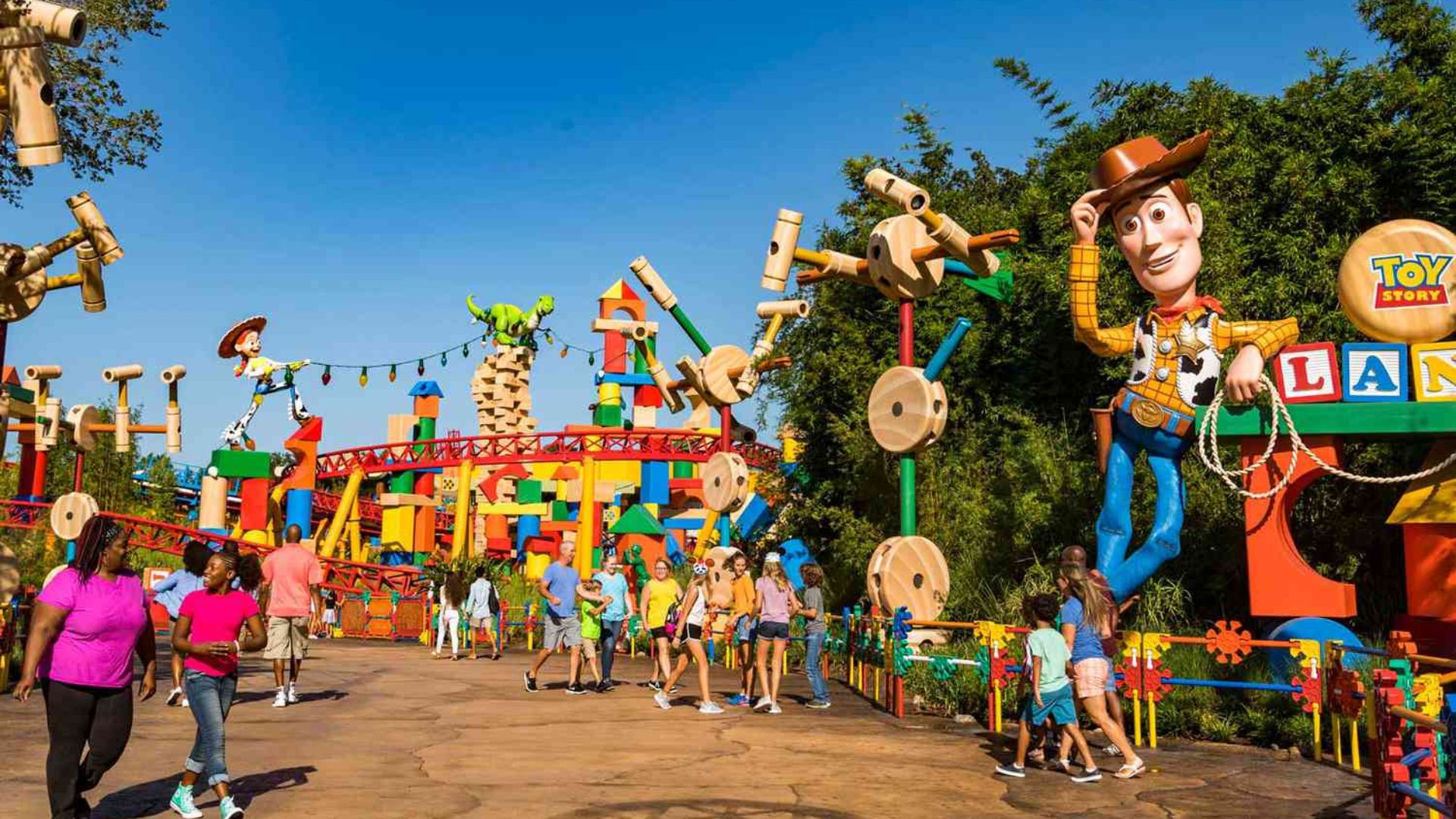 People stroll through a park alongside life-sized Toy Story characters, enjoying a vibrant outdoor atmosphere.