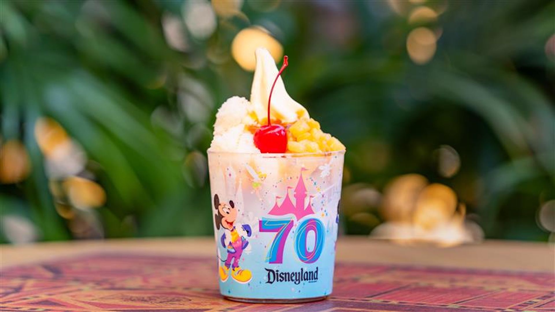 A cup of ice cream topped with a chocolate Mickey Mouse figure, set against a colorful background.