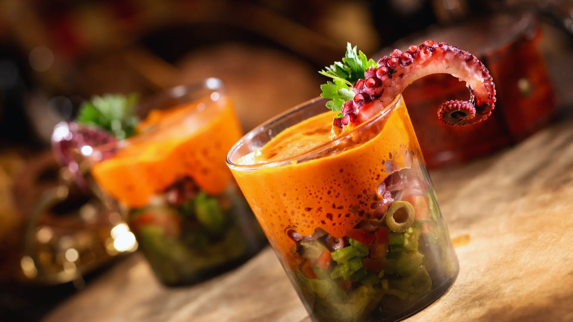 Two cocktails topped with curled octopus tentacles, served in elegant glasses on a wooden table.