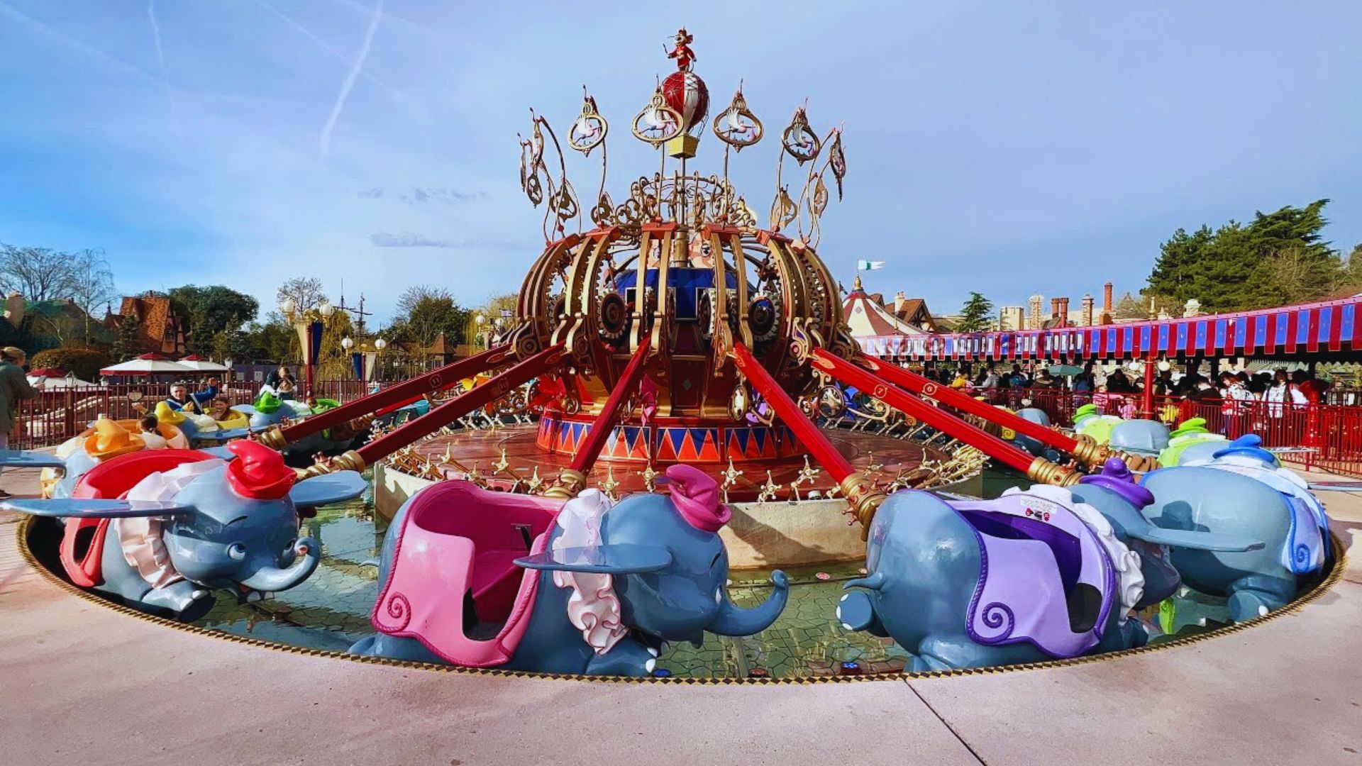 A large amusement park featuring elephants and various rides, bustling with visitors enjoying the attractions.
