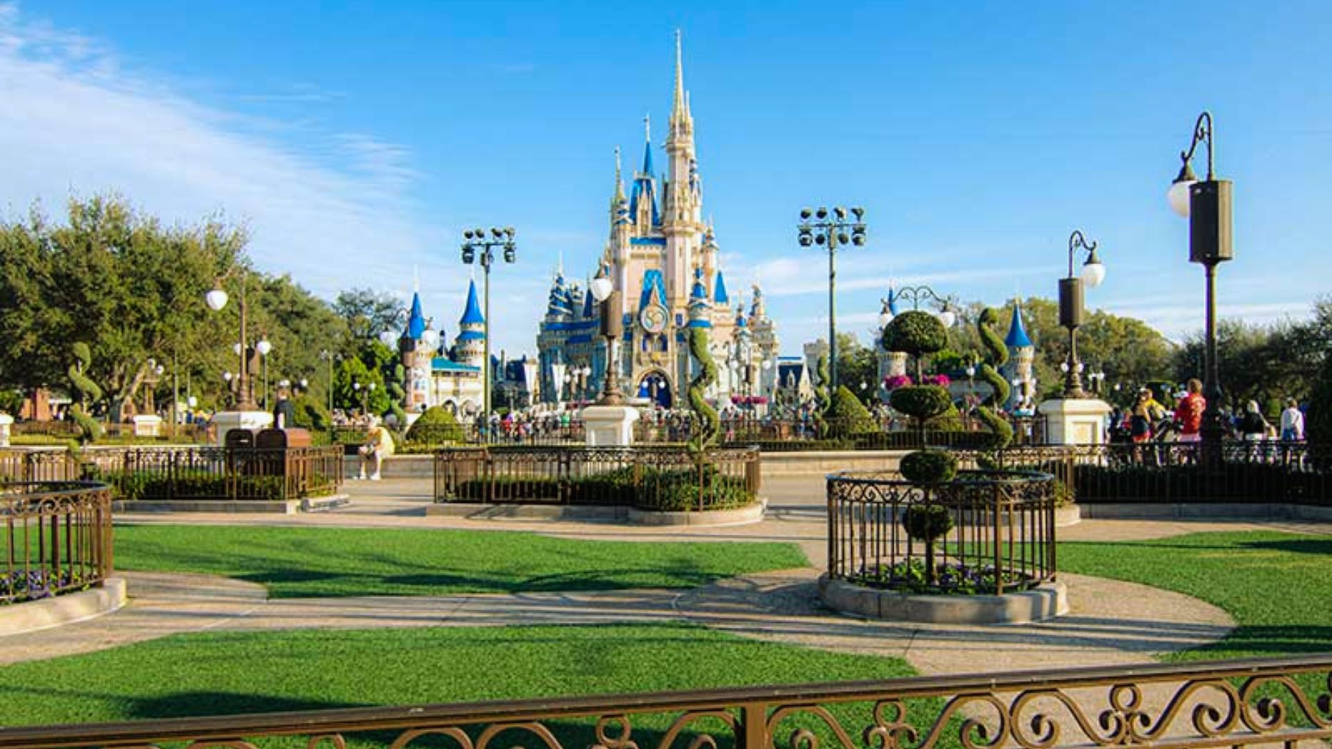 The iconic Disney World castle stands majestically in the background, surrounded by vibrant greenery and blue skies.