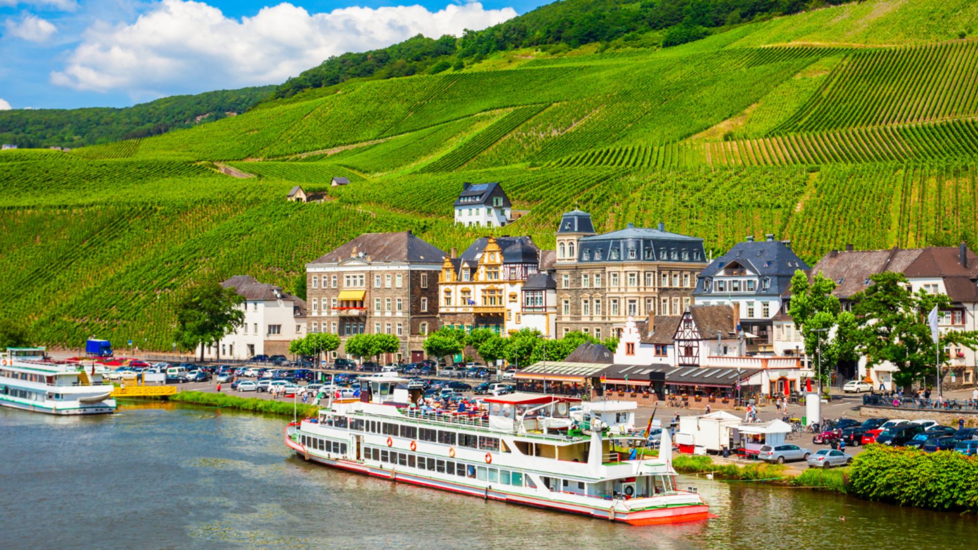 A scenic river with boats gliding on the water, framed by a lush green hillside in the background.