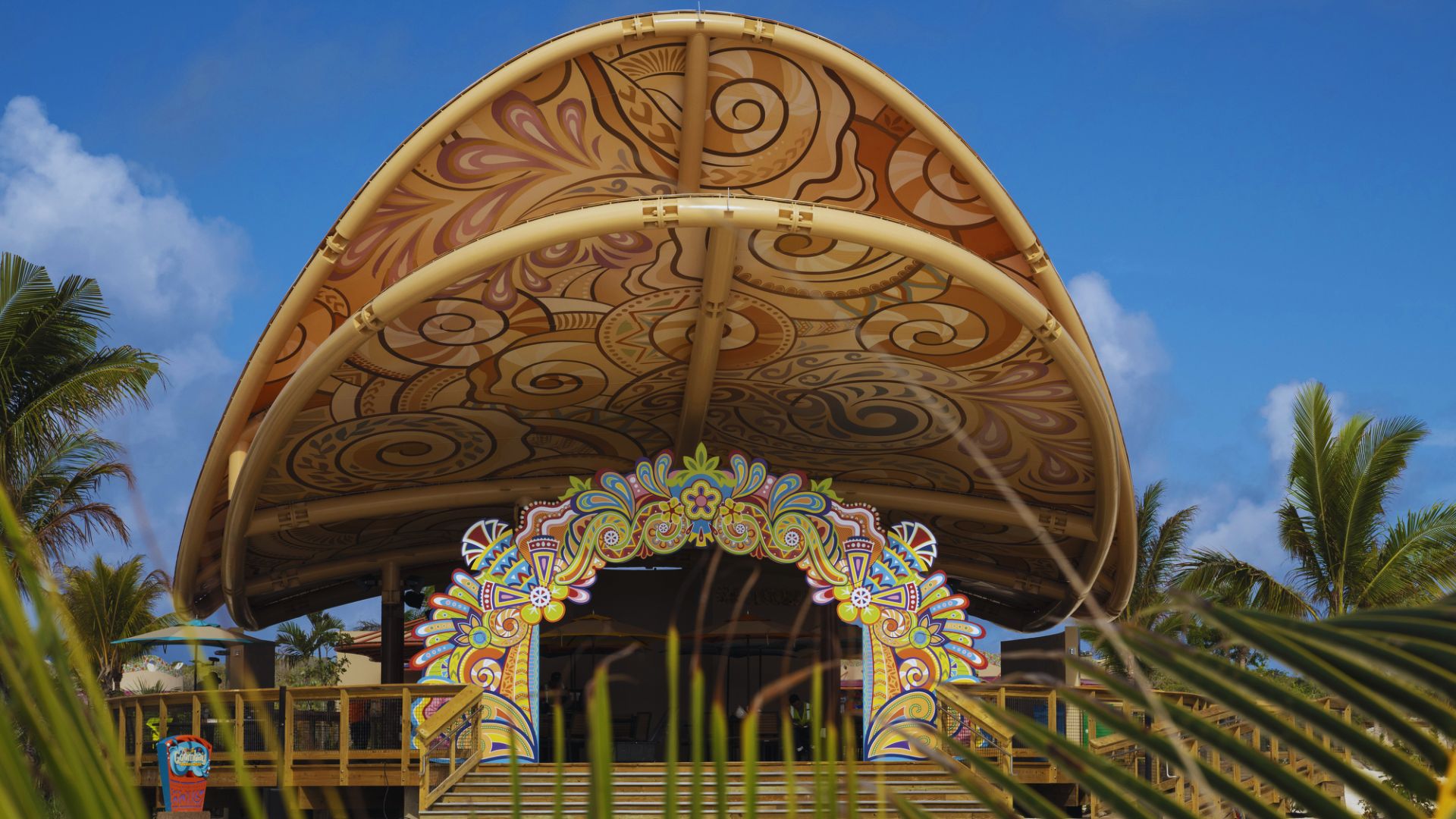 A vibrant beach structure topped with a large umbrella, surrounded by sand and ocean waves in the background.