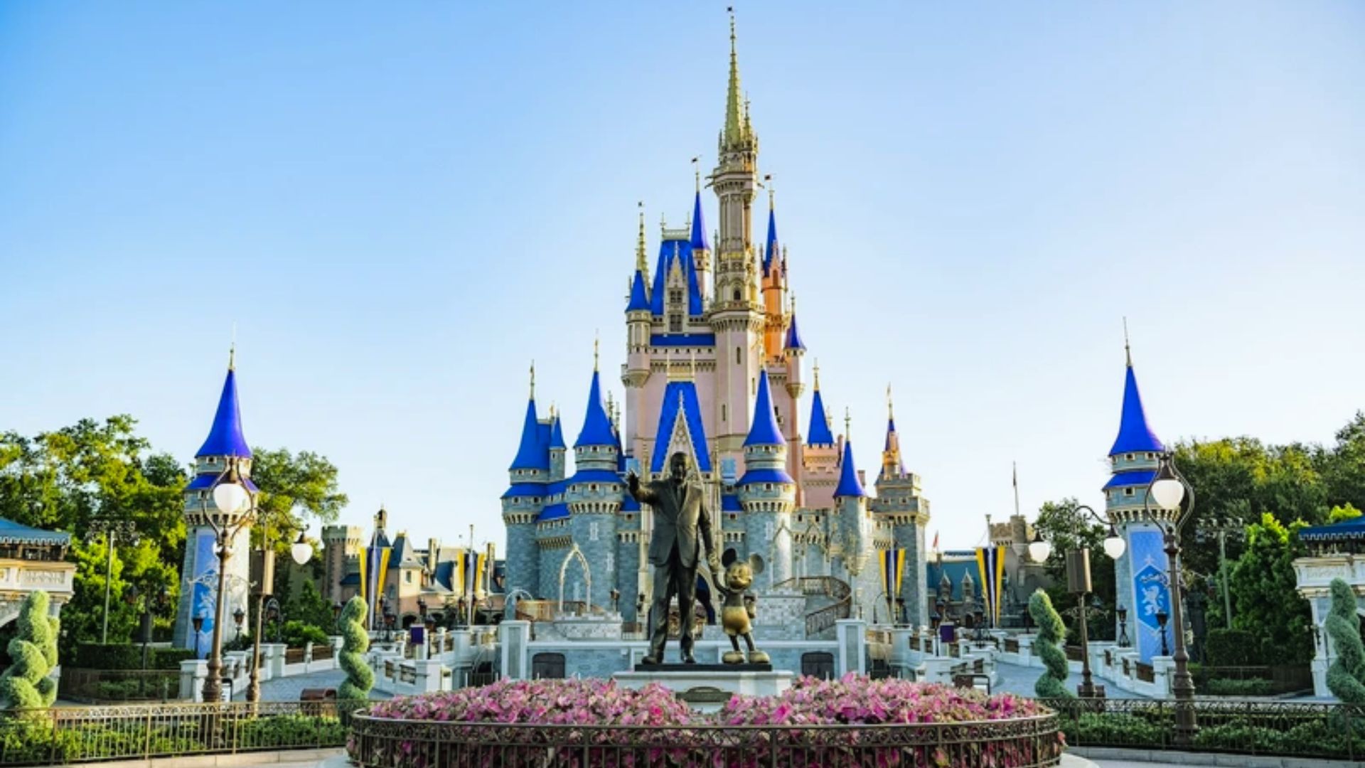 Cinderella Castle stands majestically in the background of the park, surrounded by lush greenery and vibrant attractions.