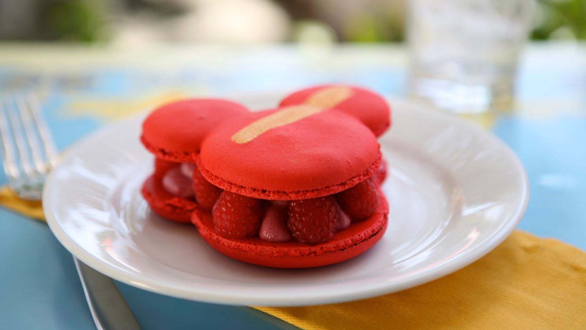 Colorful macarons shaped like Mickey Mouse, featuring his iconic ears and facial features, arranged on a decorative plate.