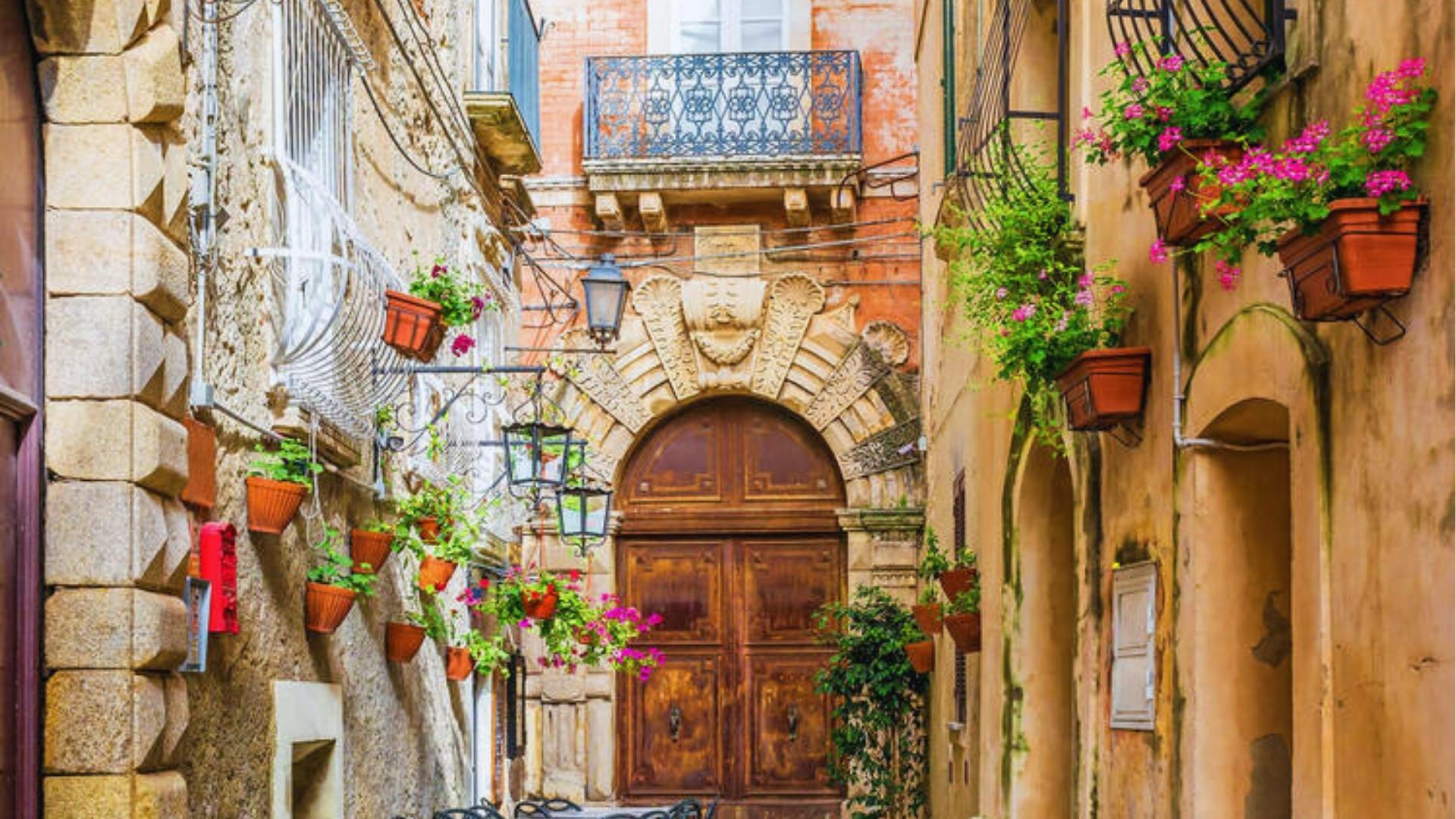 A narrow street featuring outdoor tables and chairs set up in front of a door, inviting for dining or relaxation.