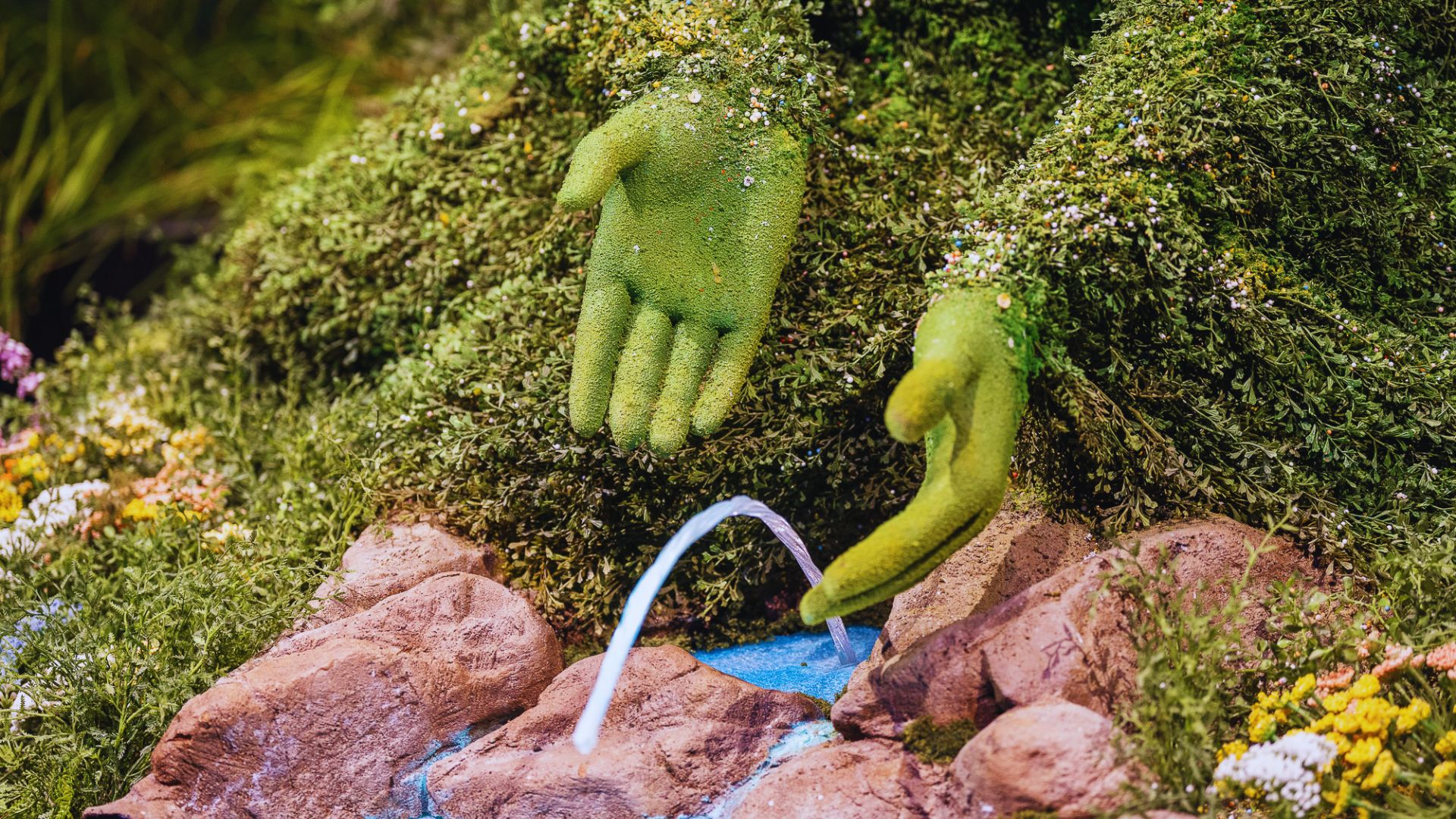 A green hand holds a water fountain, showcasing a unique blend of nature and design.