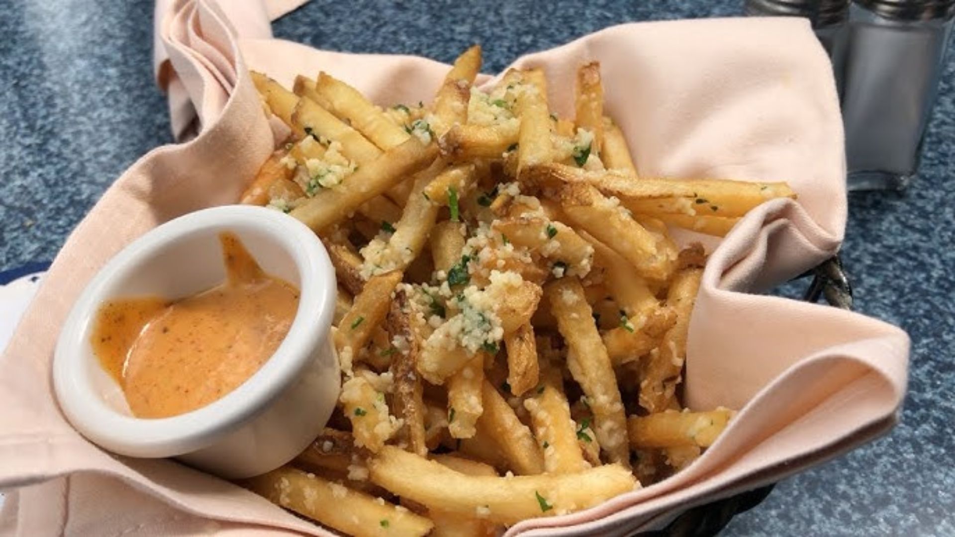 A basket filled with golden French fries accompanied by a small bowl of dipping sauce.