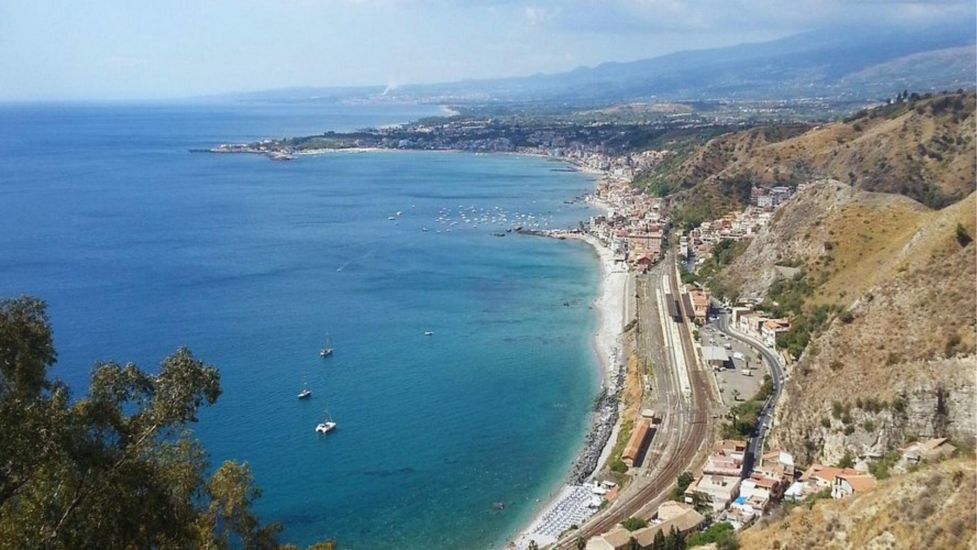 A scenic view of the coast and mountains from a hill, showcasing the natural beauty of the landscape.