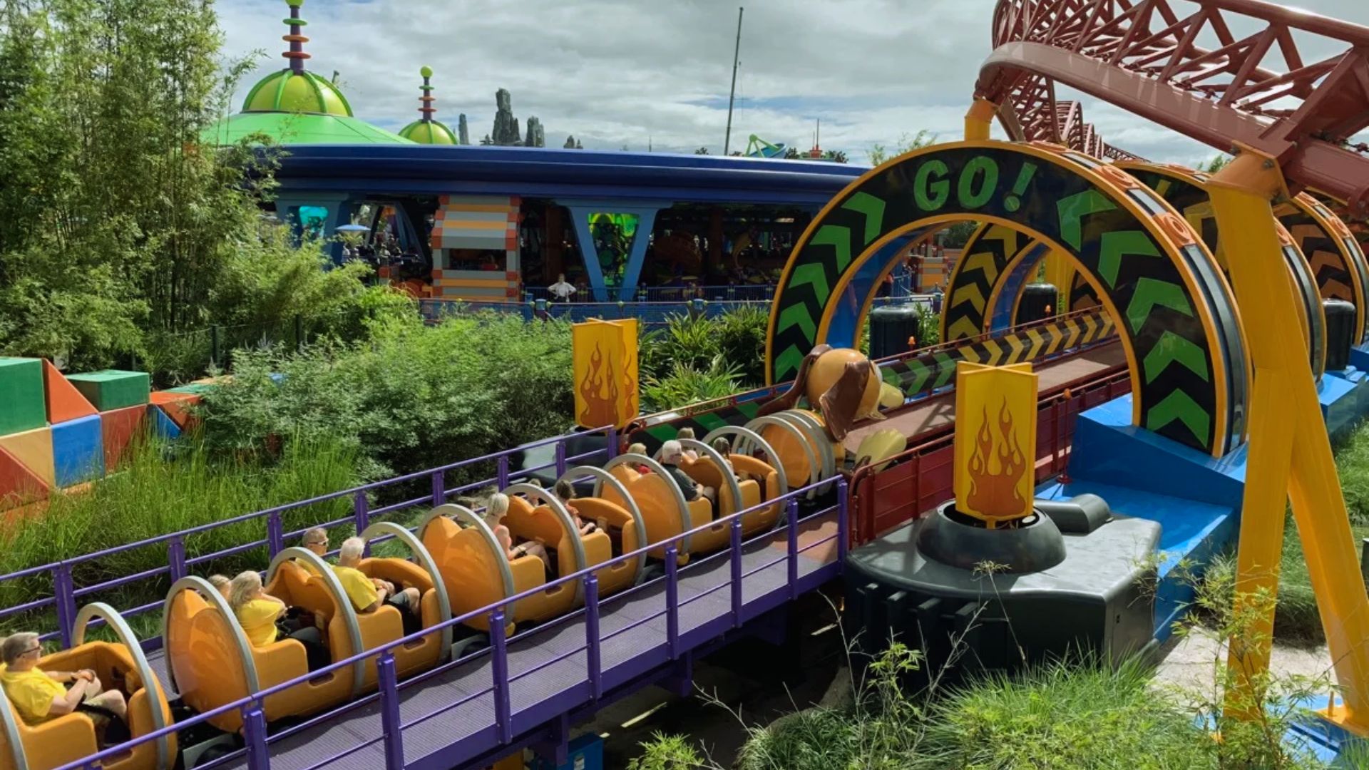 A vibrant roller coaster with colorful cars twists through a lush green landscape.