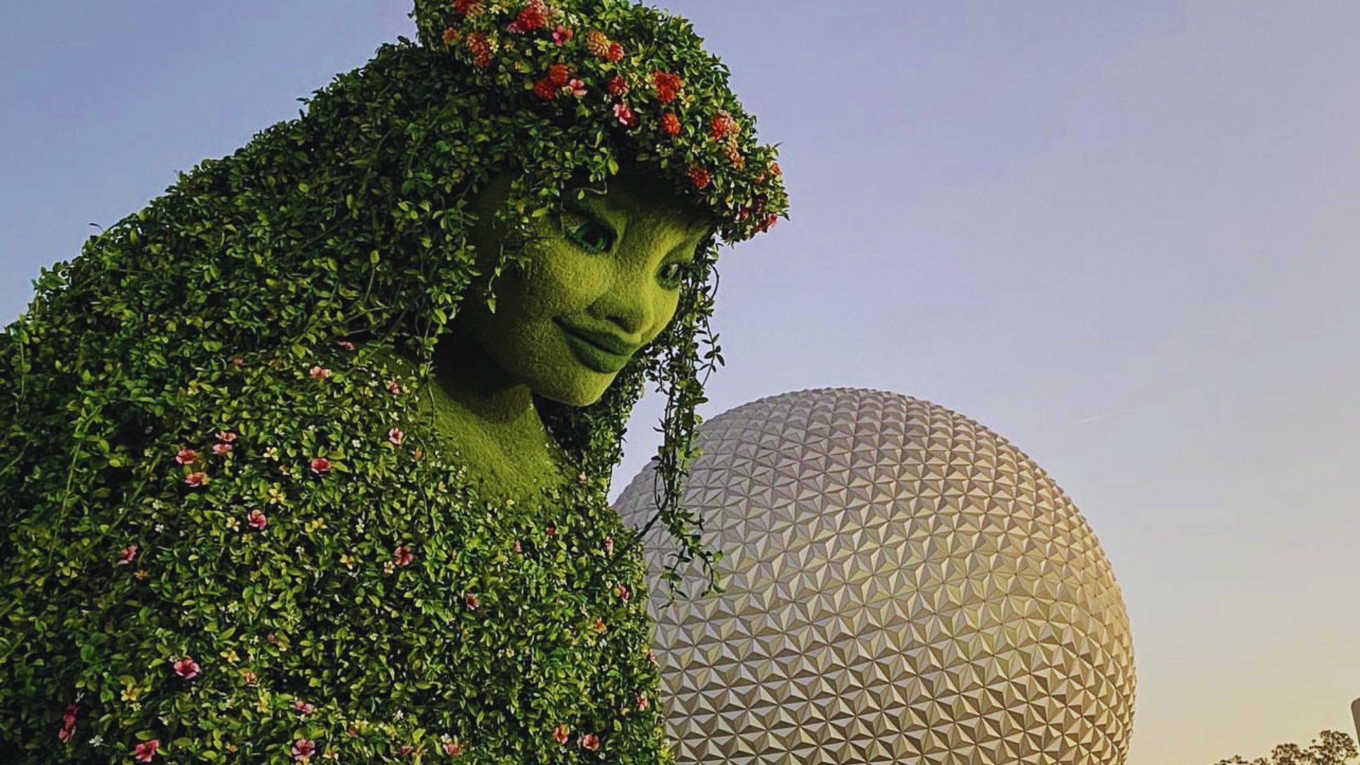 A woman wearing a green dress adorned with flowers in her hair, standing gracefully in a natural setting.