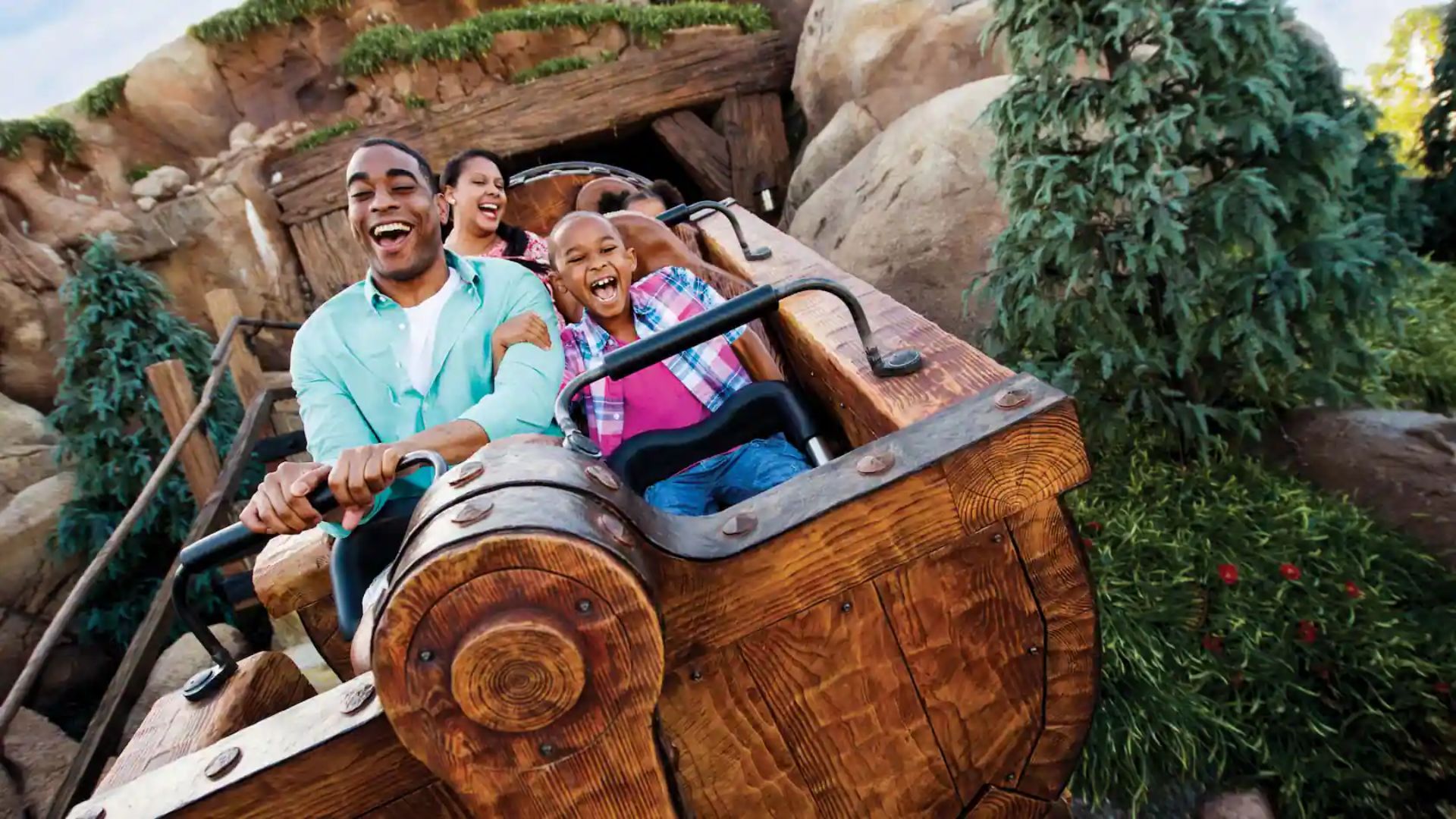 A family enjoys a thrilling ride on a wooden roller coaster at Disney's Animal Kingdom, smiling and raising their hands.