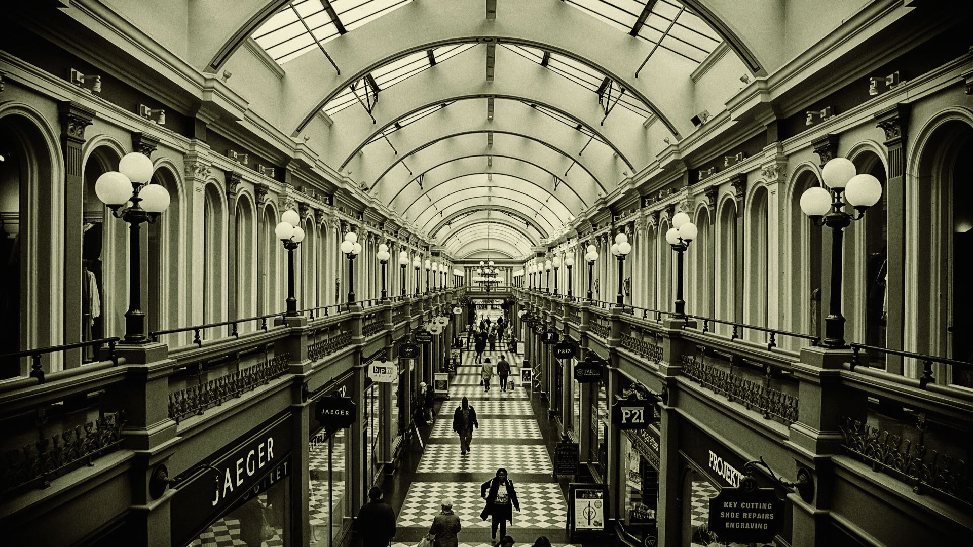 Black and white photo of a shopping mall interior, showcasing stores and shoppers in a bustling environment.