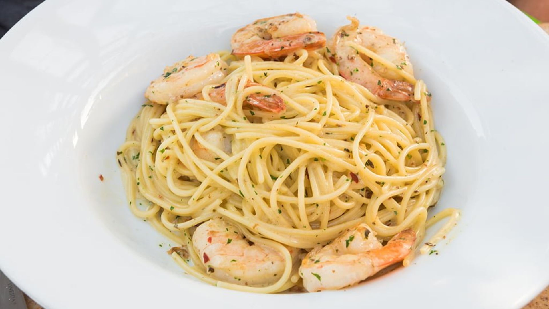 A plate of pasta topped with shrimp and garlic, garnished with herbs, served on a white dish.