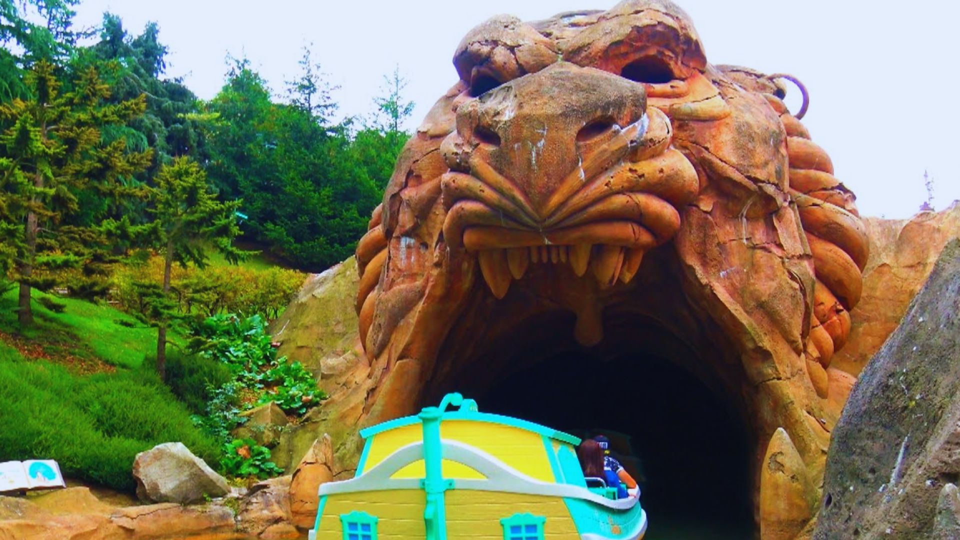 A boat floats in front of a massive cave shaped like a dragon's head, surrounded by rocky cliffs and water.