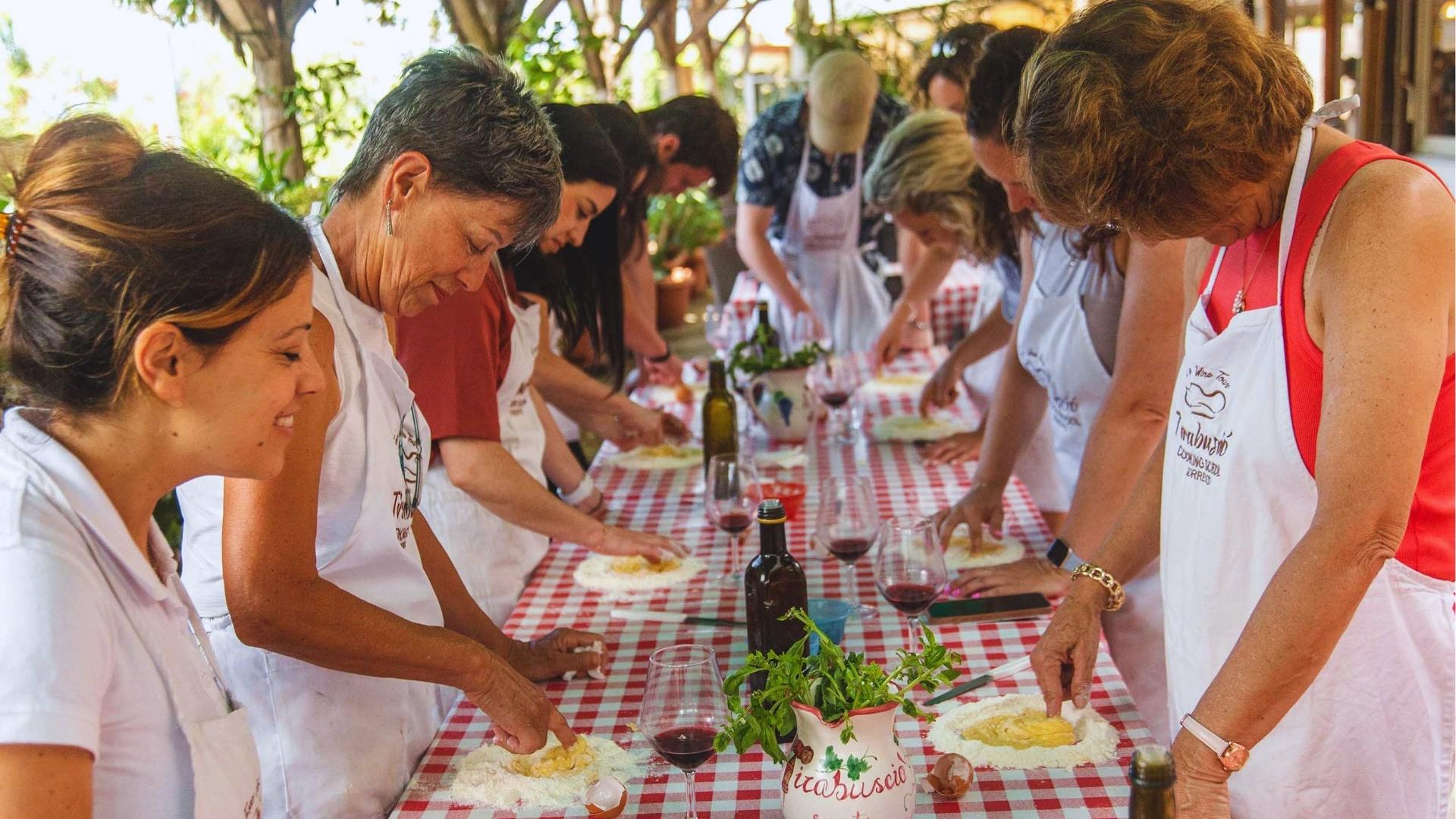 A group of women collaborating to prepare food at a table, surrounded by various ingredients and cooking utensils.