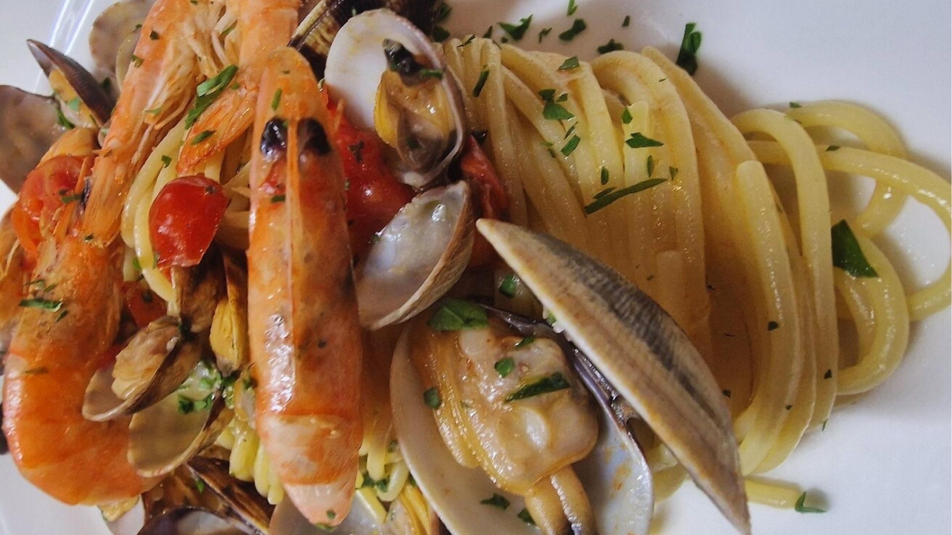 A plate of pasta topped with seafood, including clams, garnished with herbs and a drizzle of olive oil.