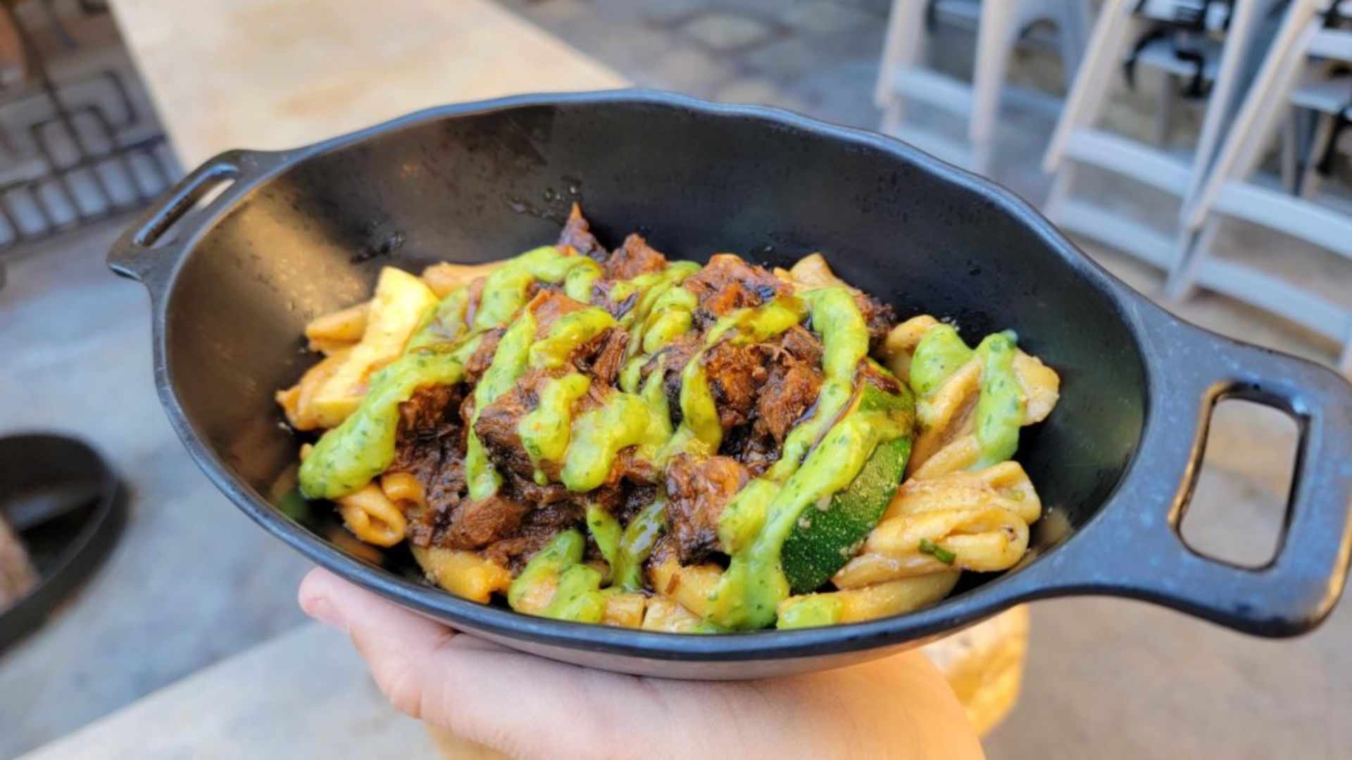 person holding a black bowl filled with food, showcasing a close-up of their hands and the bowl's contents.