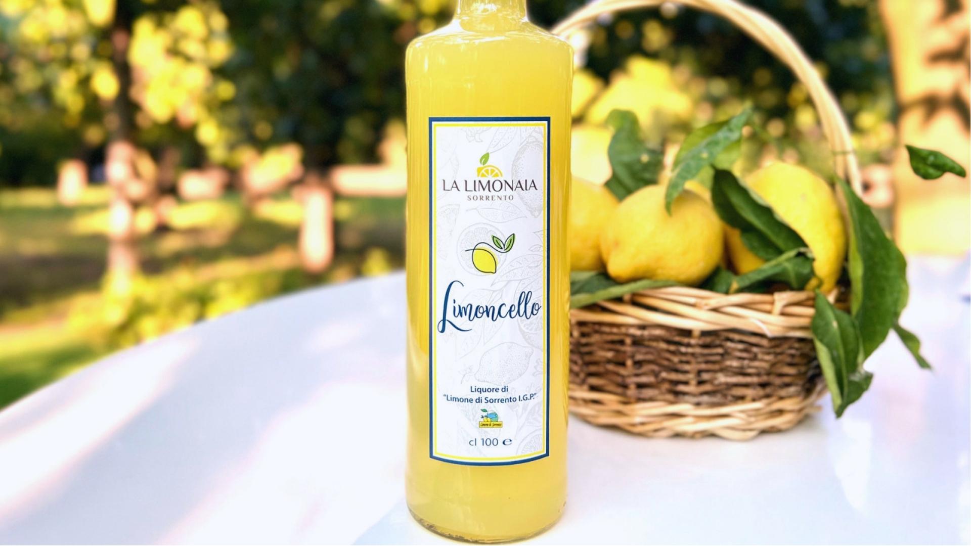A bottle of lemonade beside a basket filled with fresh lemons, showcasing a refreshing summer drink.