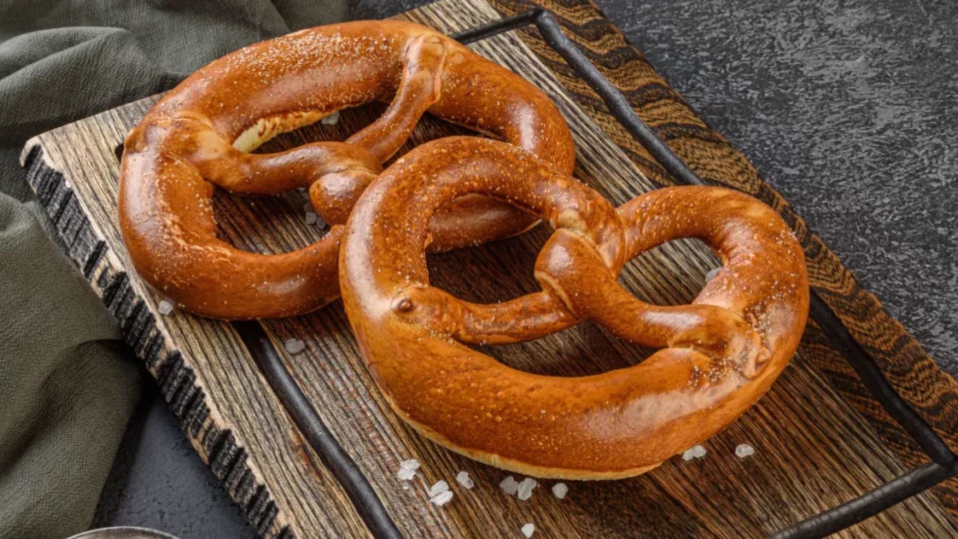 Two salted pretzels resting on a wooden cutting board, showcasing their twisted shape and golden-brown color.