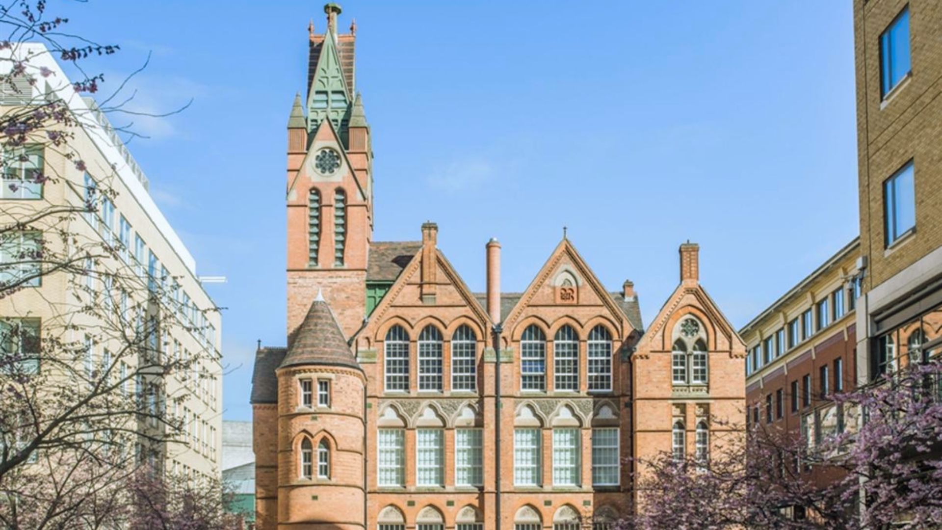 A large red brick building featuring a prominent clock tower against a clear sky.