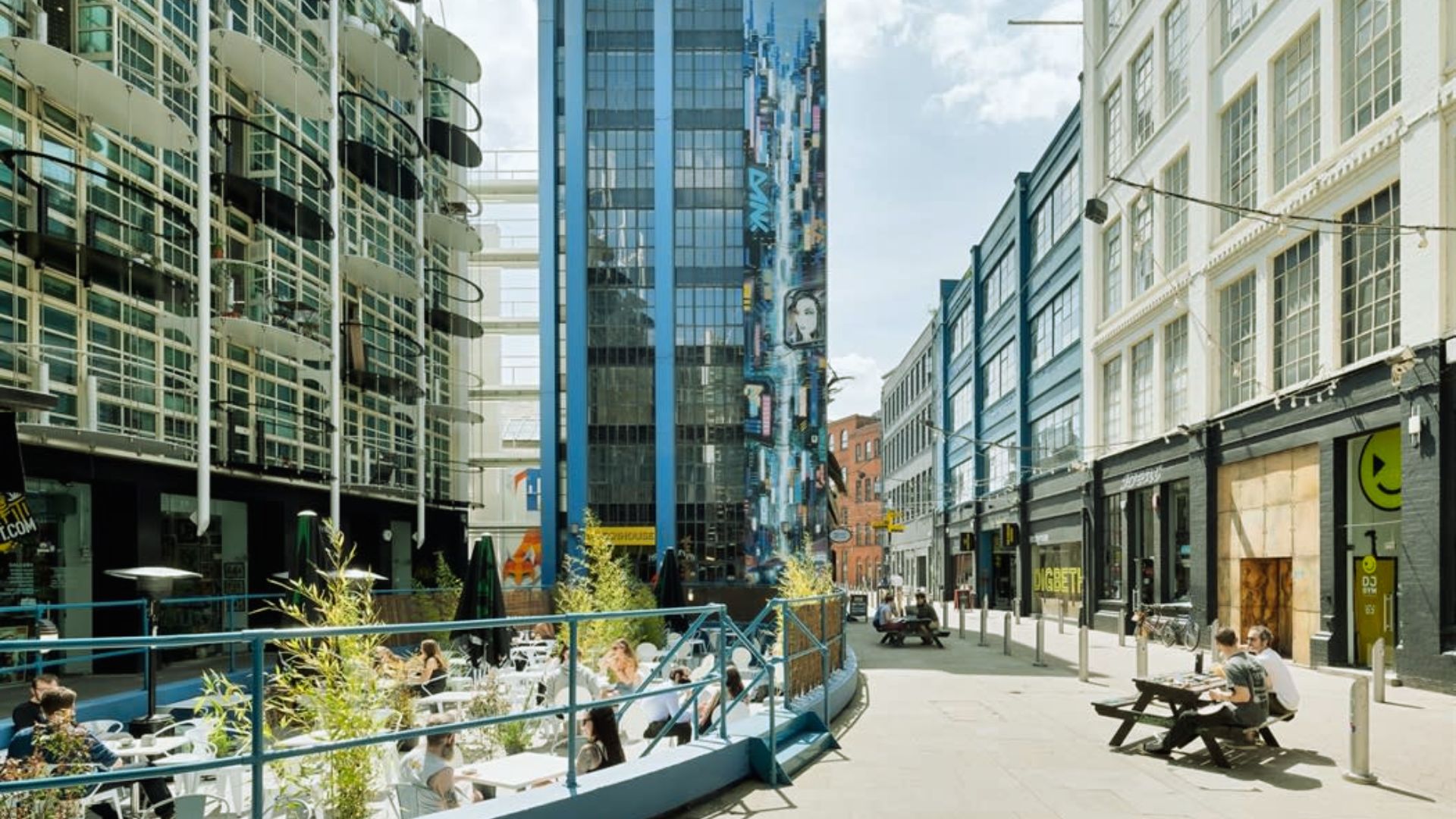 A bustling city street with people dining outdoors at tables, enjoying their meals in a lively atmosphere.