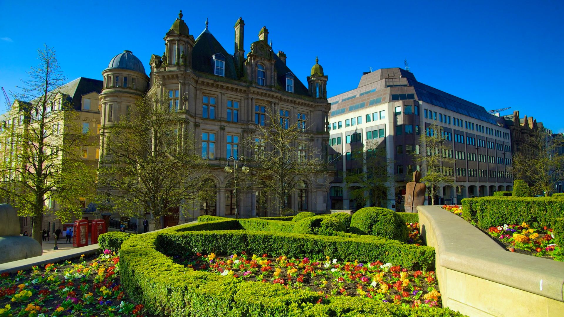 A large building featuring a clock tower, surrounded by a well-maintained garden.
