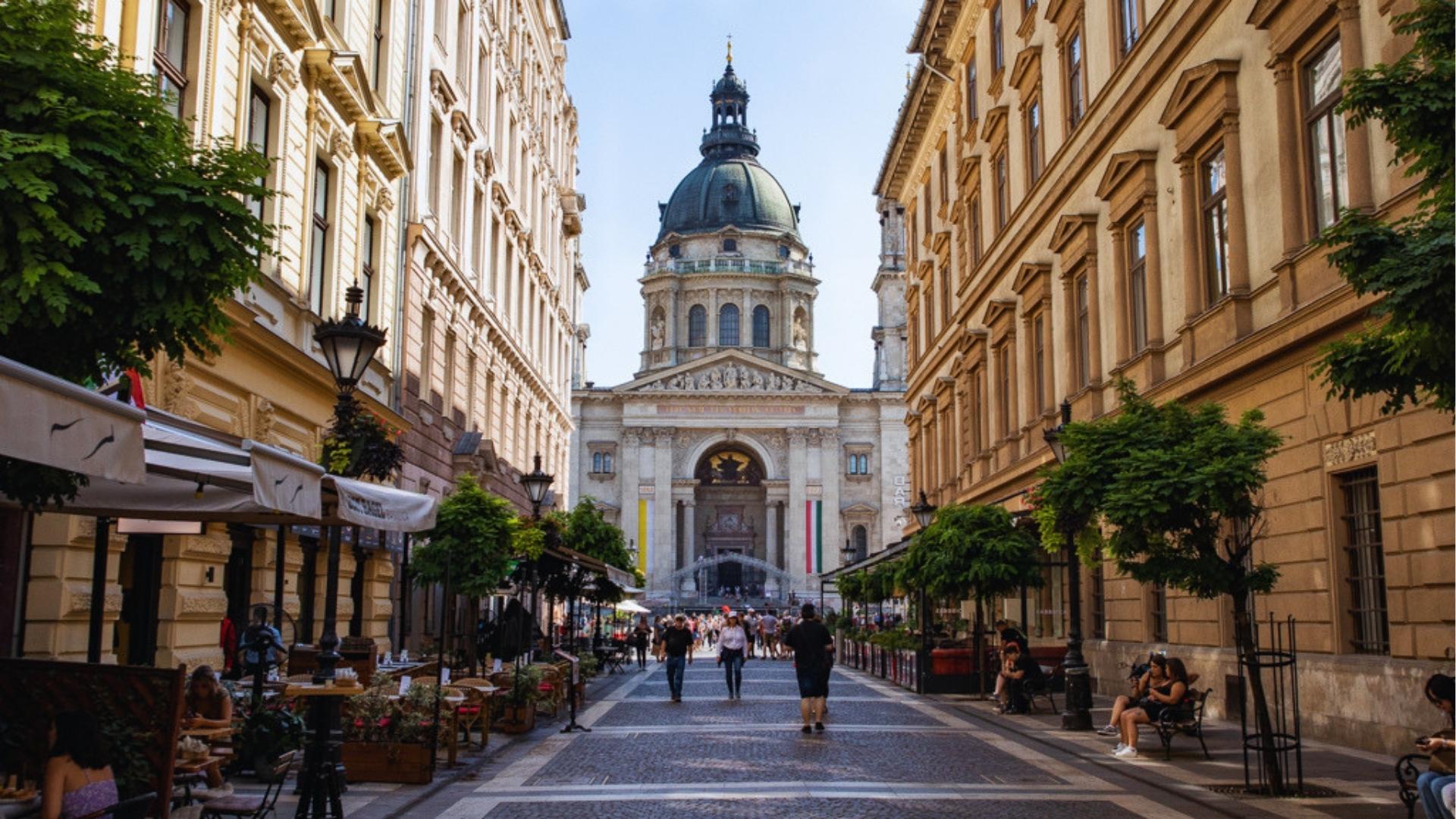 A bustling street in Budapest with people walking and enjoying outdoor seating at cafes.