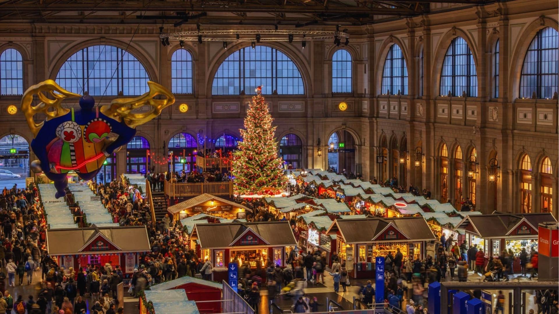 Christmas market bustling with visitors inside Munich's train station, featuring festive decorations and stalls.