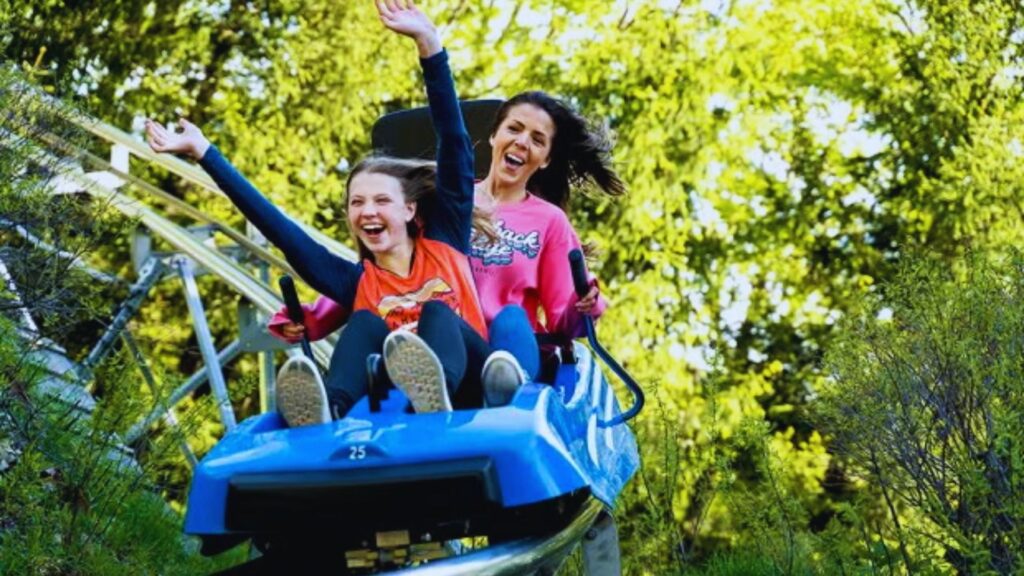 Two girls joyfully screaming as they ride a roller coaster, their hair flying in the wind.