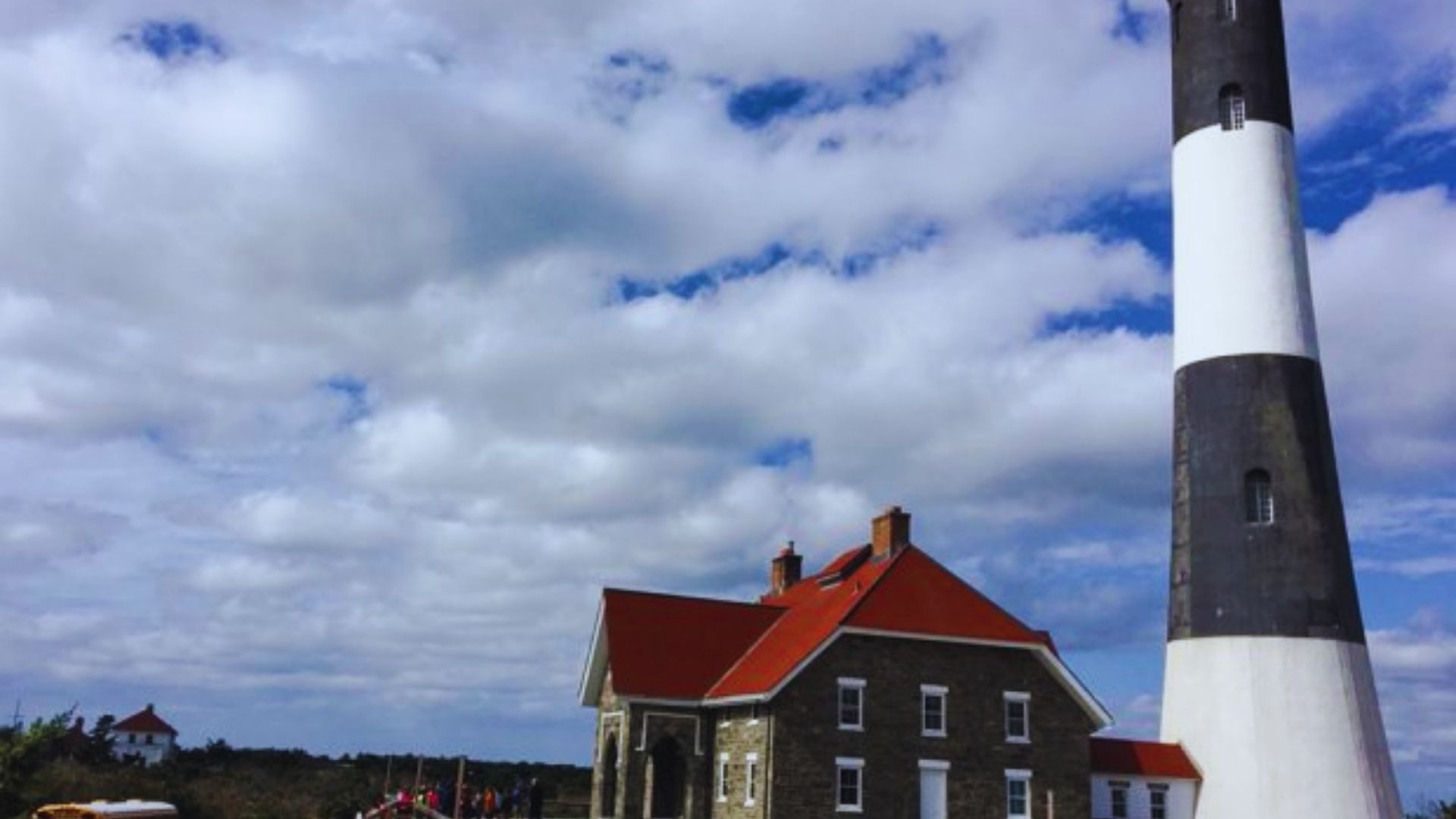 A large white and black lighthouse with a striking red roof against a clear blue sky.