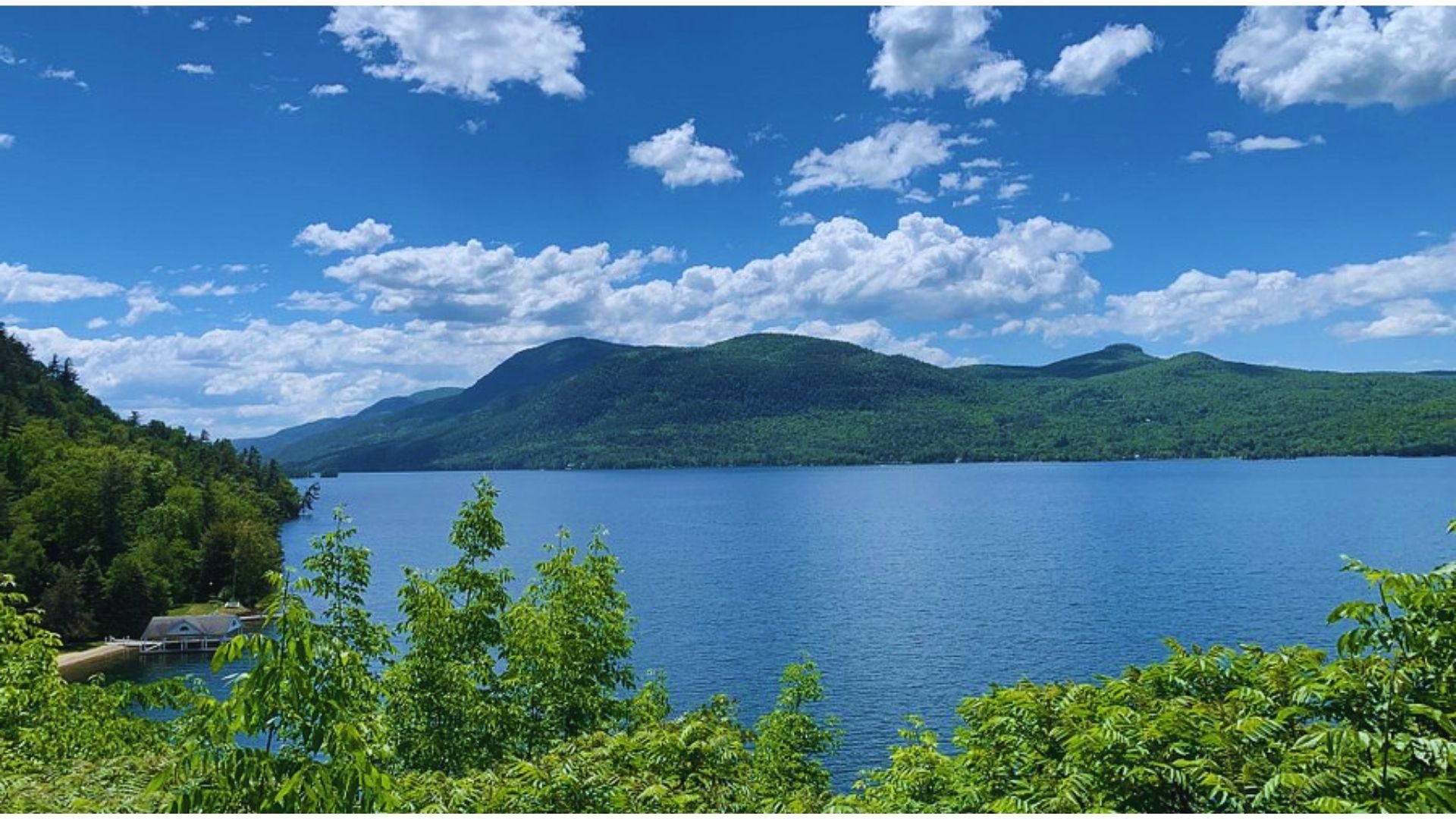 A serene lake bordered by lush trees and majestic mountains under a clear blue sky.