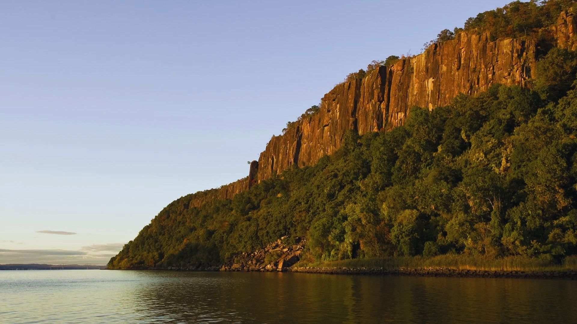 A large rock formation stands beside a flowing river, showcasing natural beauty and rugged terrain.