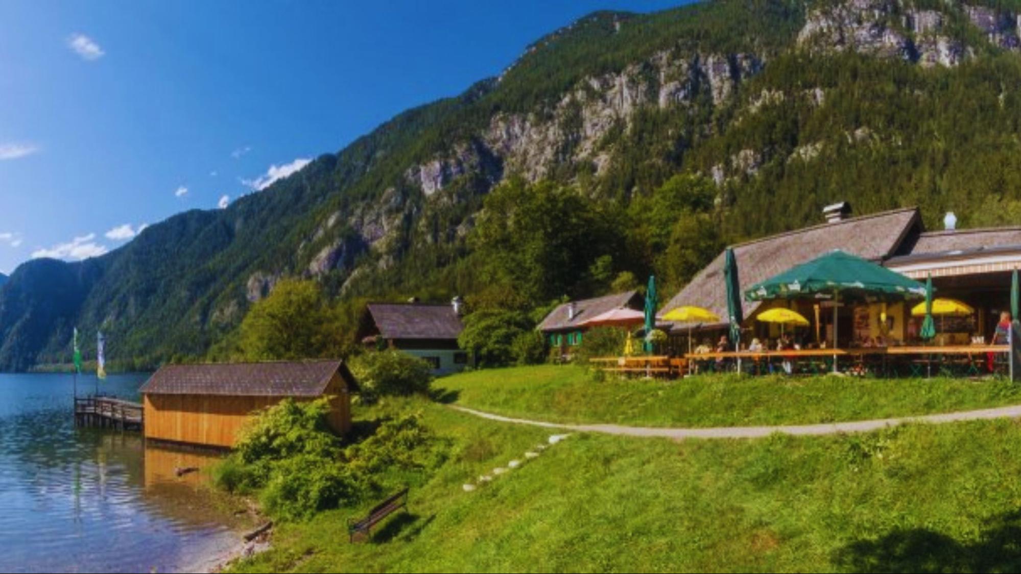 A serene lake with a restaurant on its shore and a majestic mountain rising in the background.