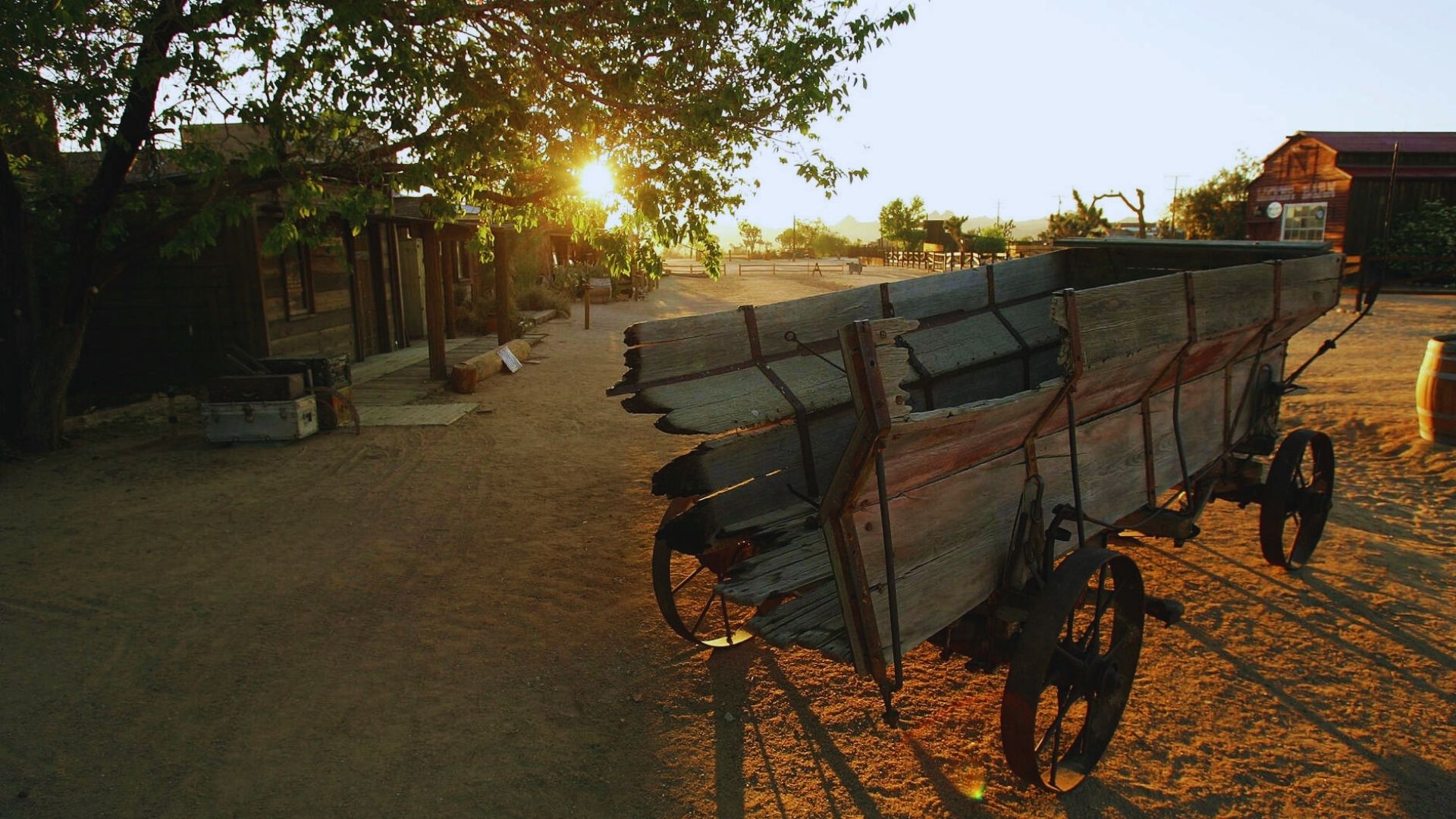 An old wagon parked on a dirt road, surrounded by sparse vegetation and a clear blue sky.