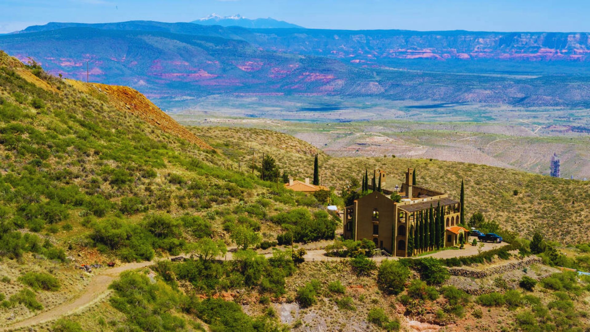 A church perched on a hill overlooks a lush valley, surrounded by greenery and distant mountains.