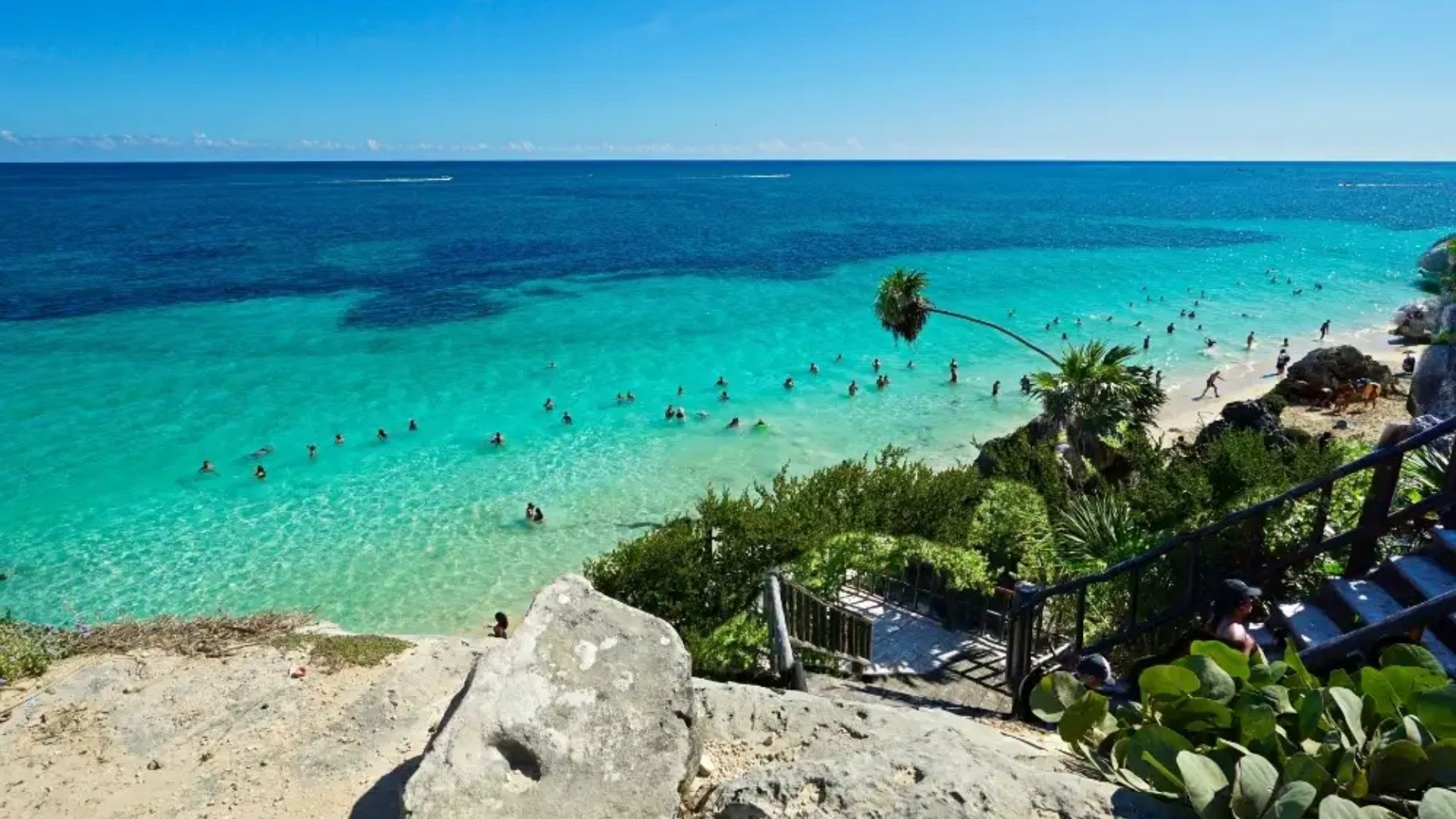 A sunny beach scene with people swimming in the clear water, enjoying the warm weather and vibrant atmosphere.