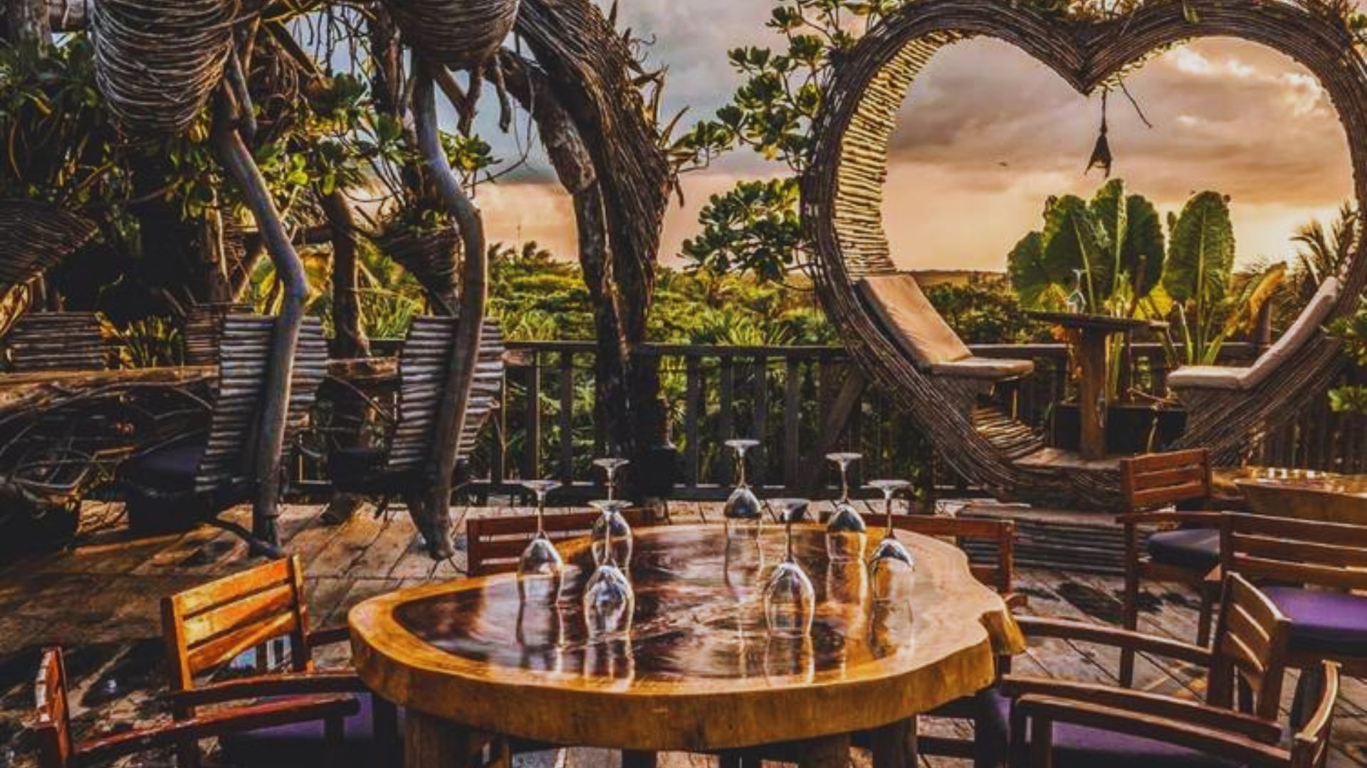A sunset casts warm hues over a wooden deck featuring a heart-shaped table, creating a romantic atmosphere.
