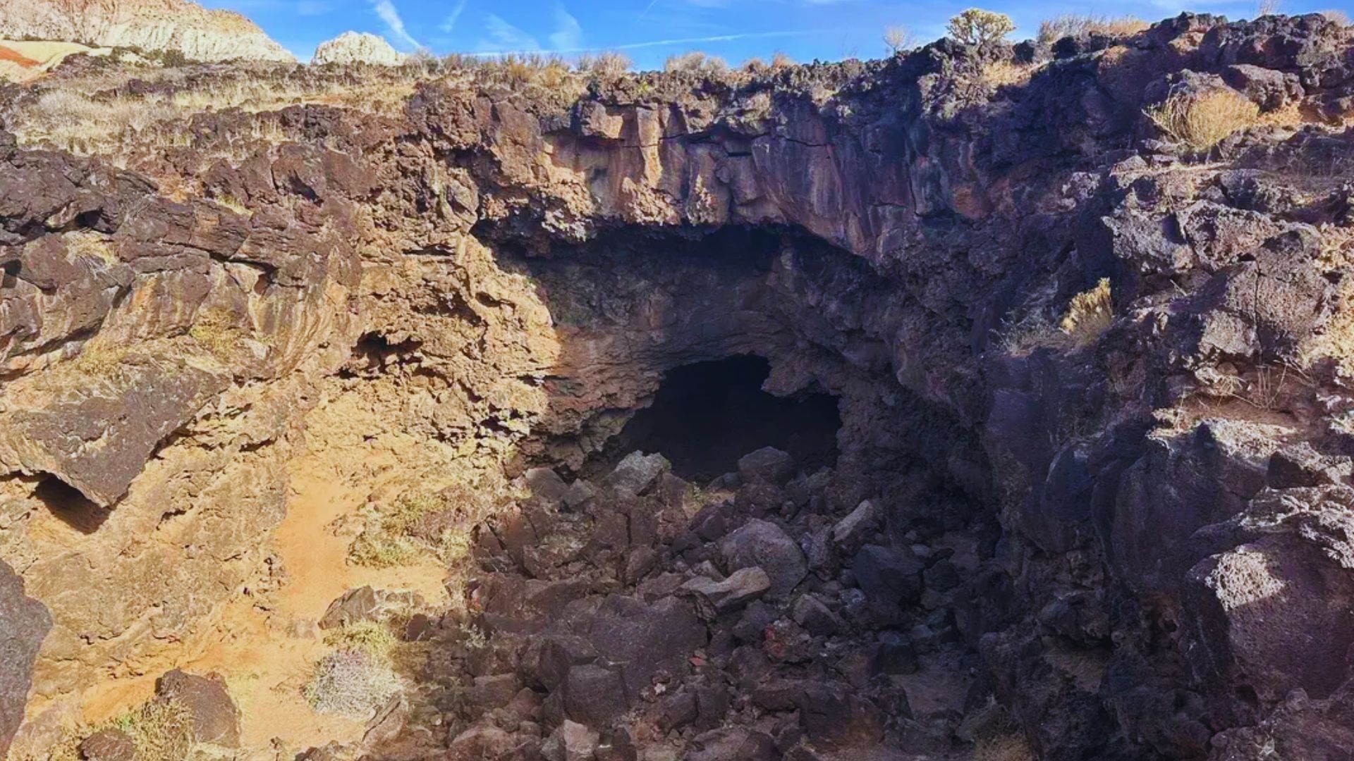 A desert cave under a clear blue sky, showcasing the contrast between the rocky terrain and the vibrant sky above.