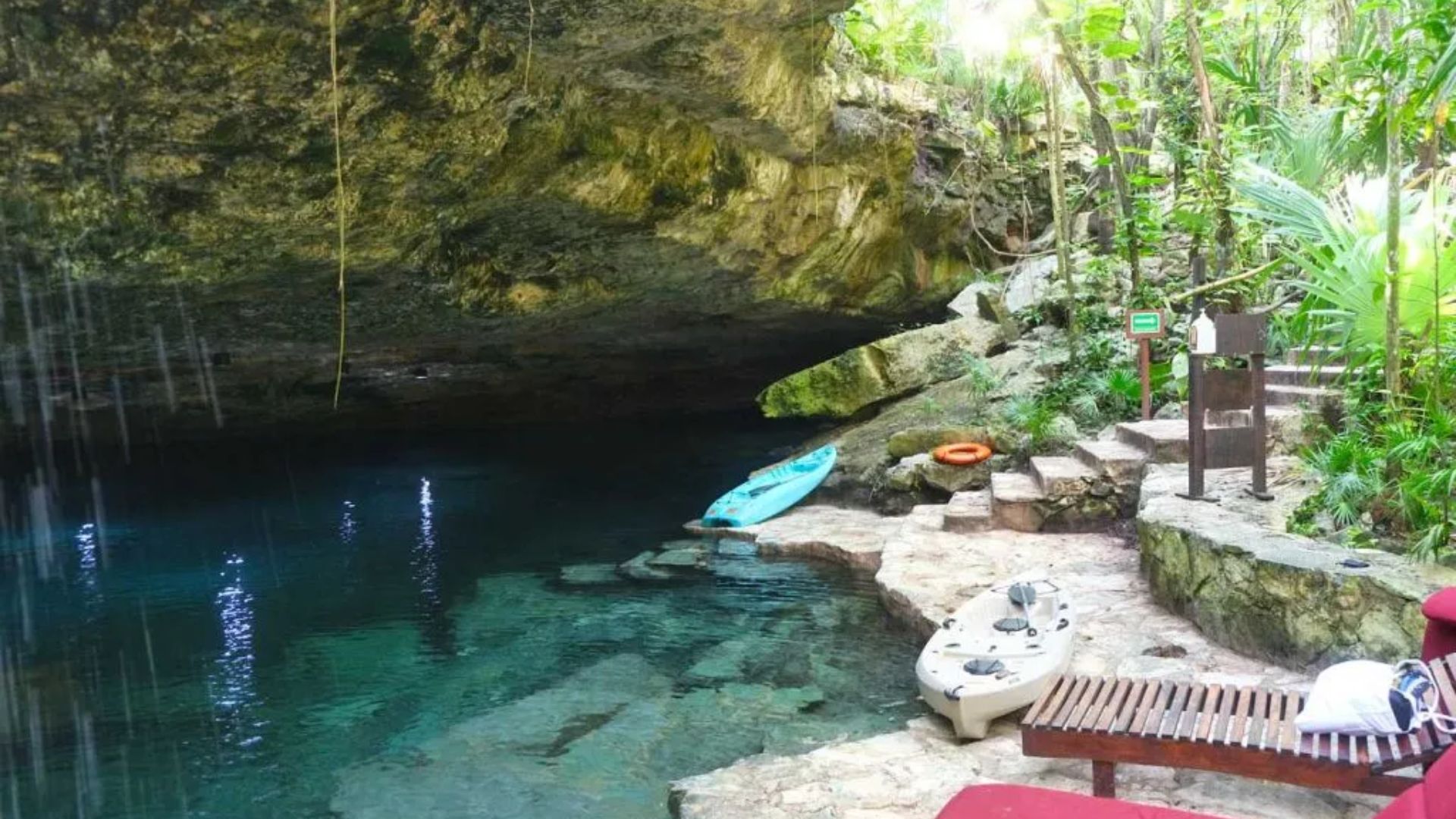 A serene cave pool featuring a kayak floating in the center, surrounded by rocky walls and dim lighting.