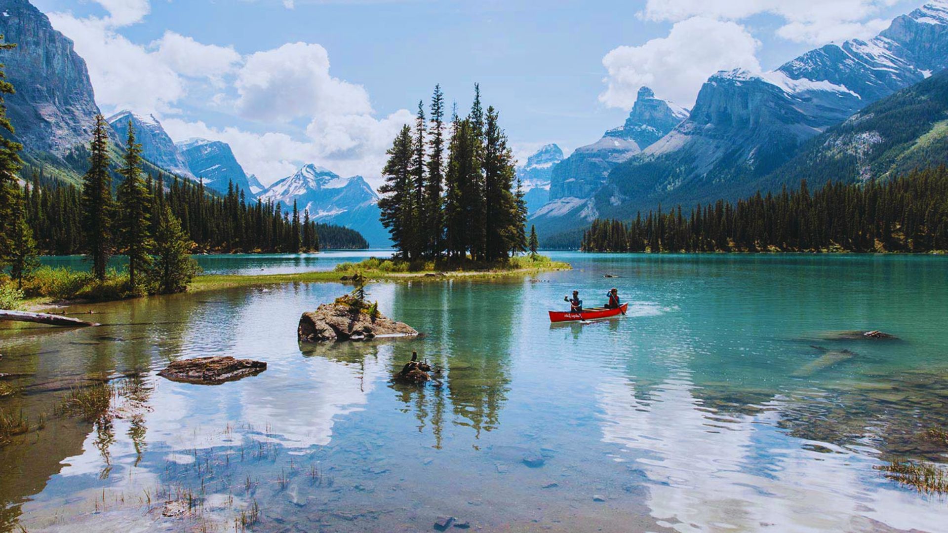 A canoe glides across a serene lake surrounded by the majestic mountains of Banff National Park.