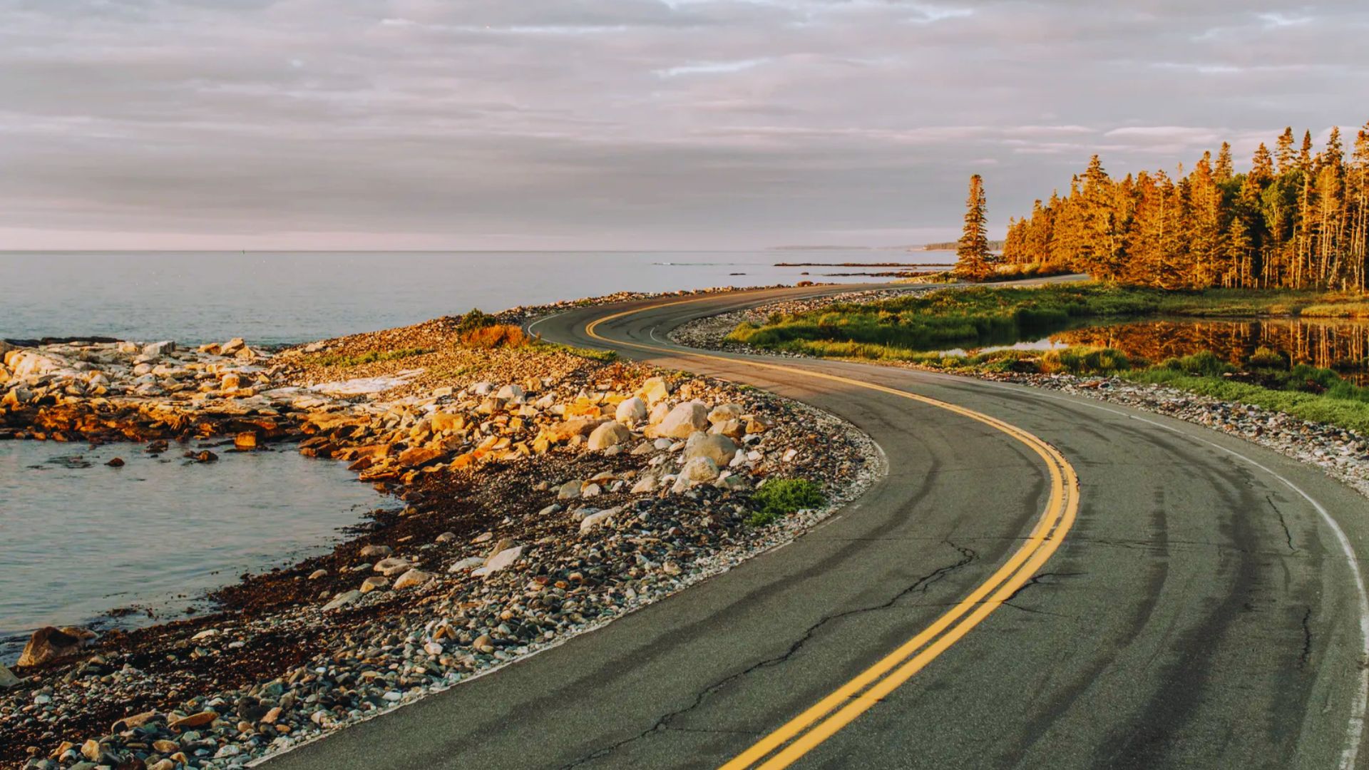 A winding road through majestic mountains alongside a sparkling ocean, showcasing a stunning natural landscape.