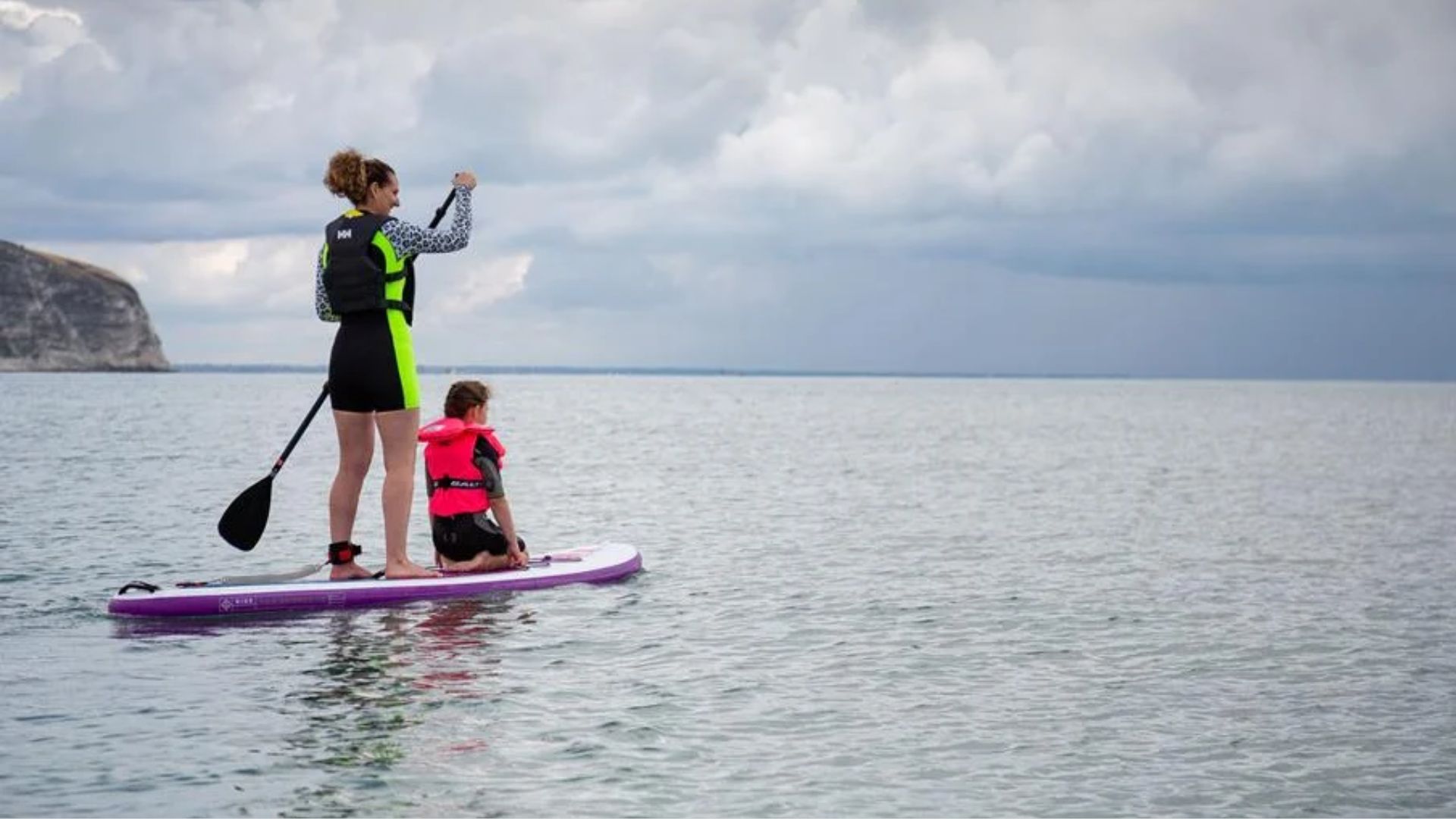 A woman and a child enjoy paddle boarding together on a sunny day in the ocean.
