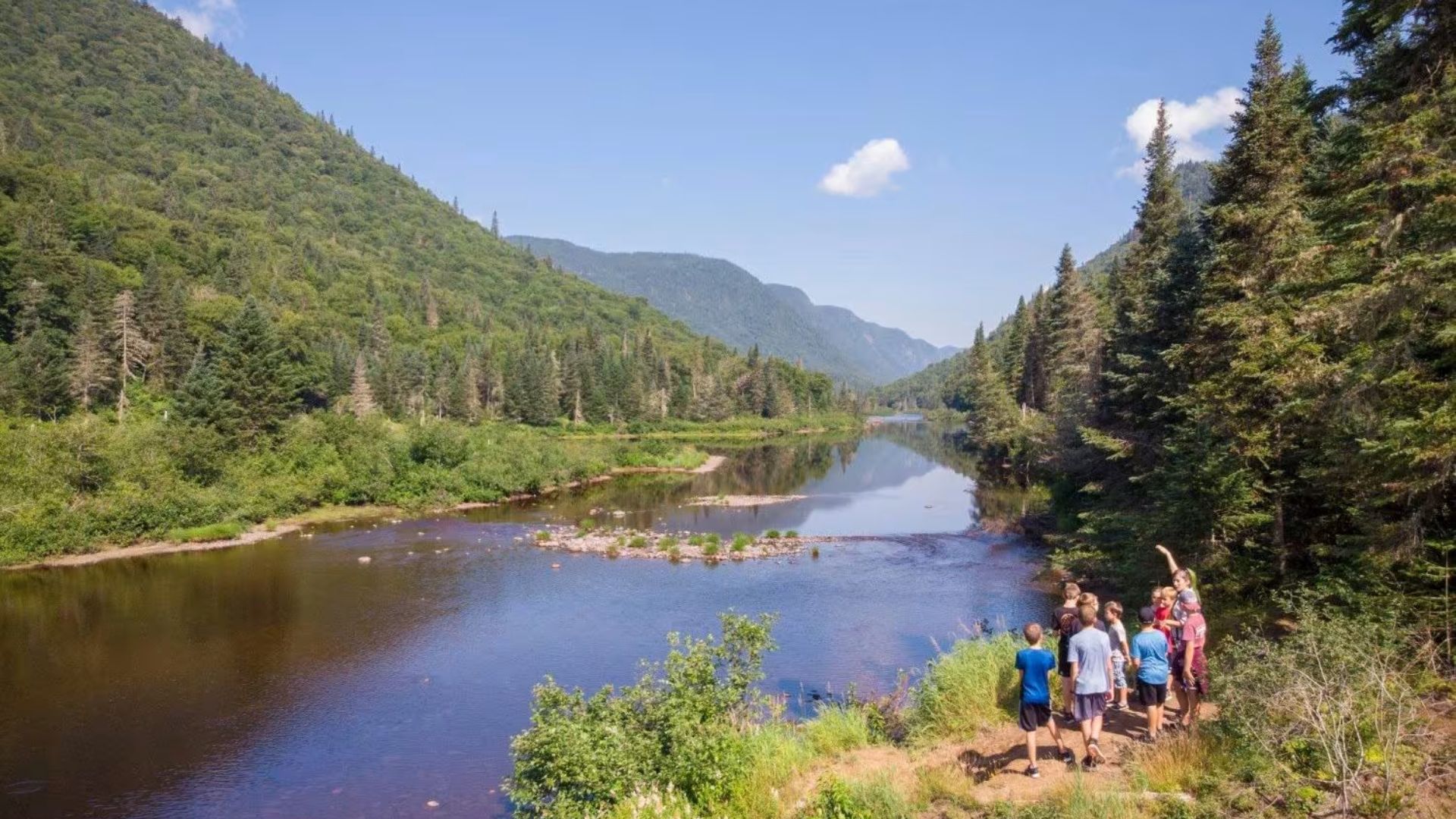 People are gathered on a trail, enjoying the view of a river winding through the landscape.
