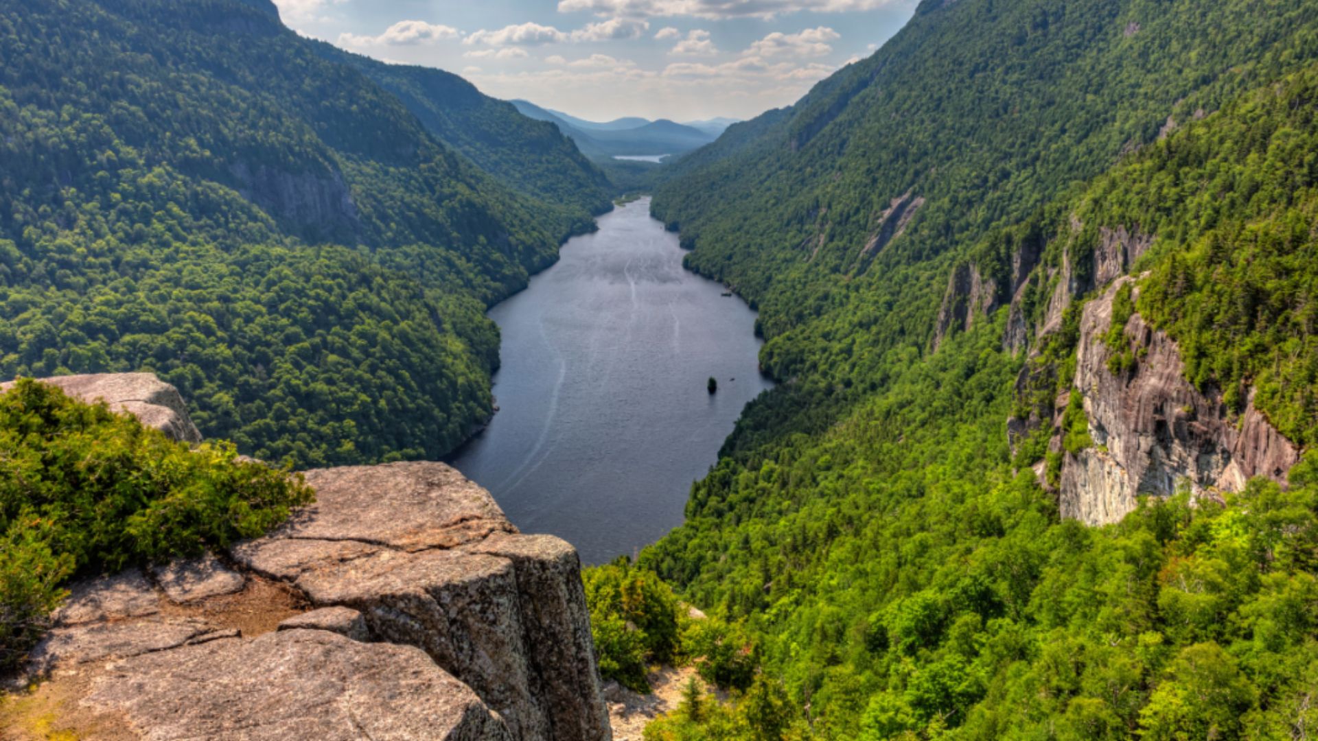 A panoramic view from a mountain peak, showcasing a winding river below surrounded by lush greenery.