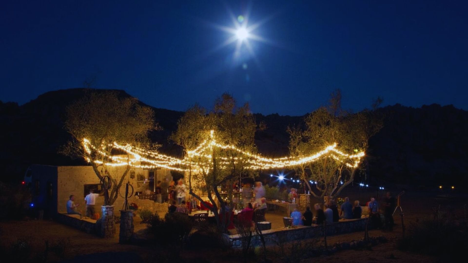 A wedding party celebrates under a starry night sky, surrounded by twinkling lights and joyful guests.